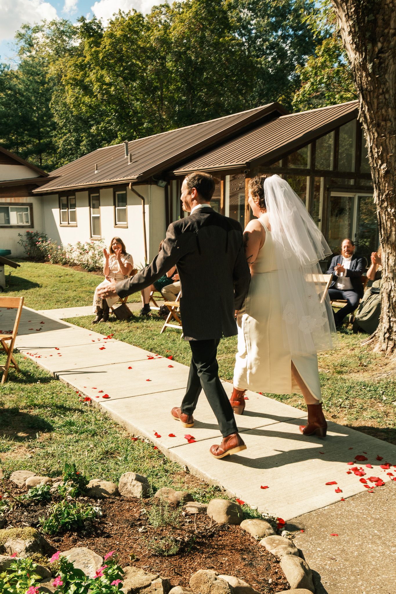 Bride and groom walk back down the aisle together after outdoor wedding ceremony with rose petals.
