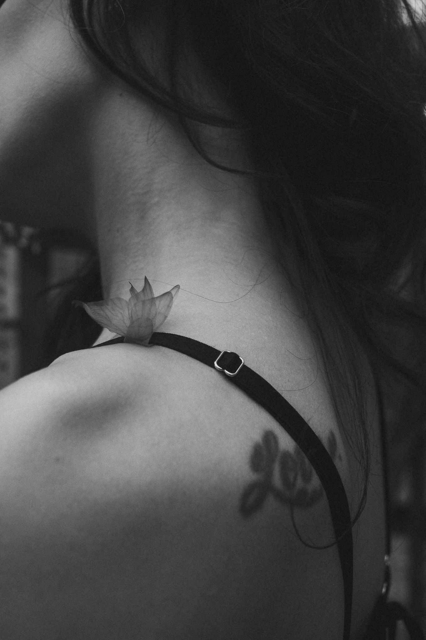 Black and white close-up of woman's shoulder and neck featuring small lotus and floral tattoos.