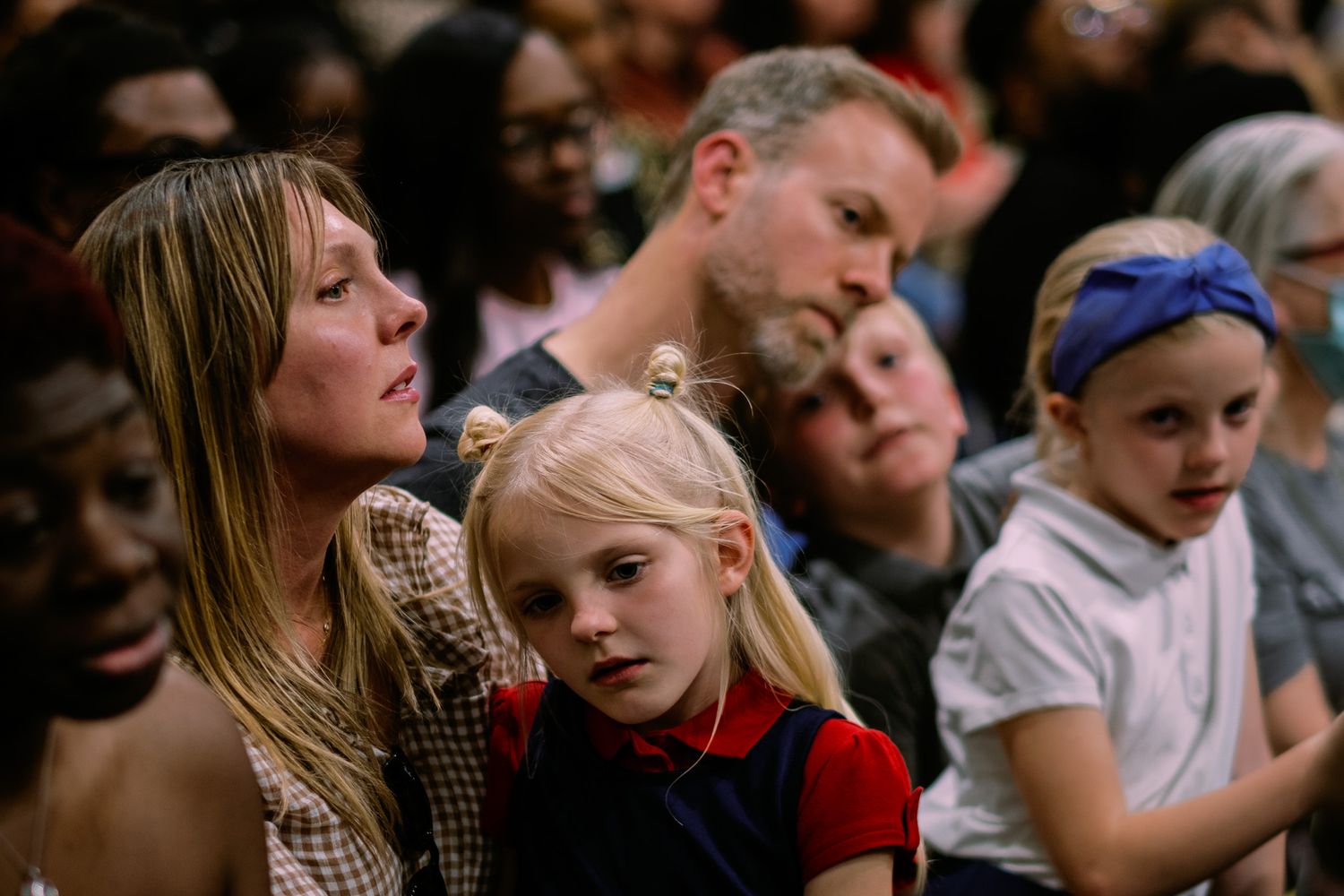 Family with children sitting together attentively watching an event in a crowded indoor venue.