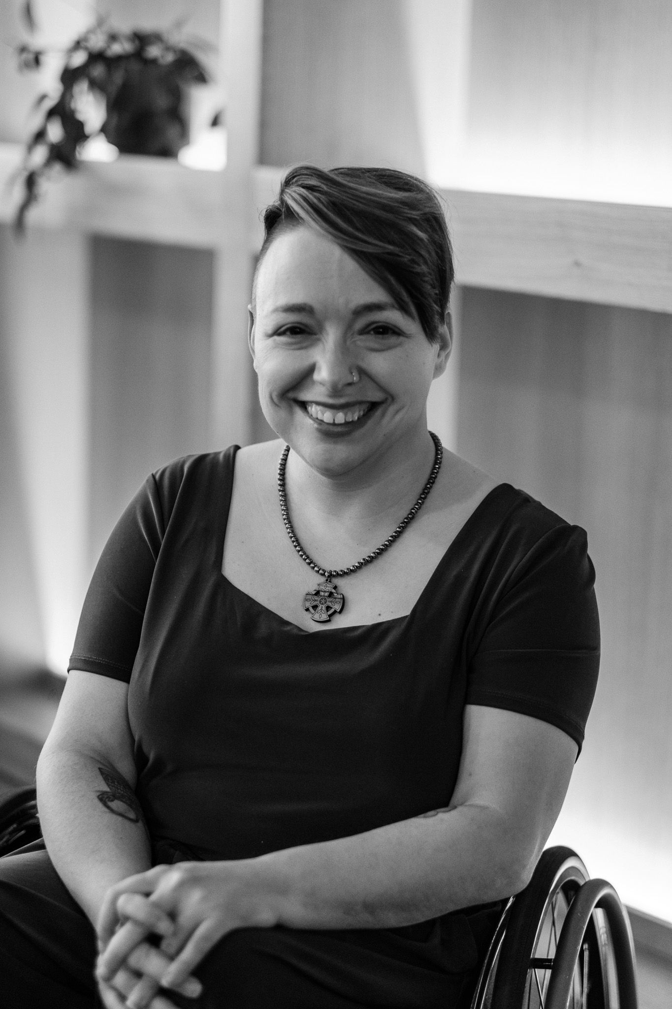 Smiling woman in a wheelchair wearing a black dress and statement necklace in a modern interior.