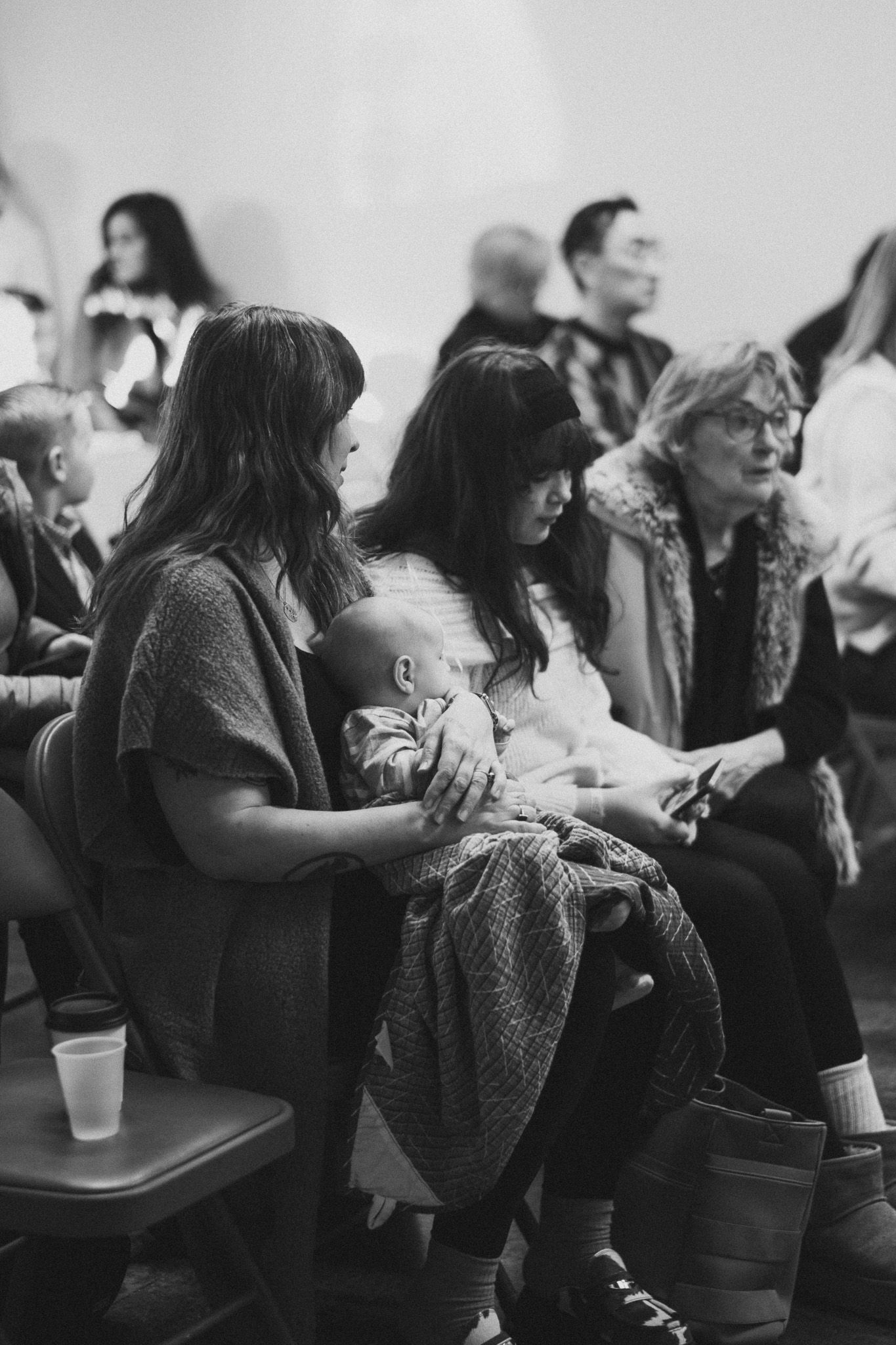 Black and white photo of a woman holding a sleeping baby while seated in an audience at a music event.