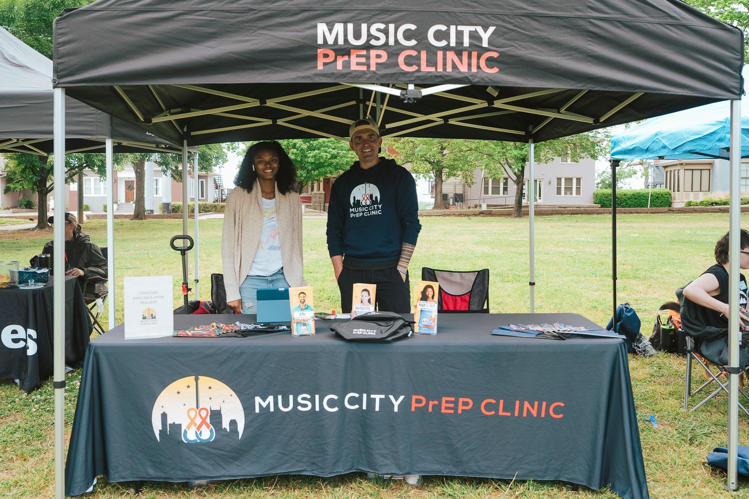 Two people standing at Music City PrEP Clinic information booth at an outdoor community event.