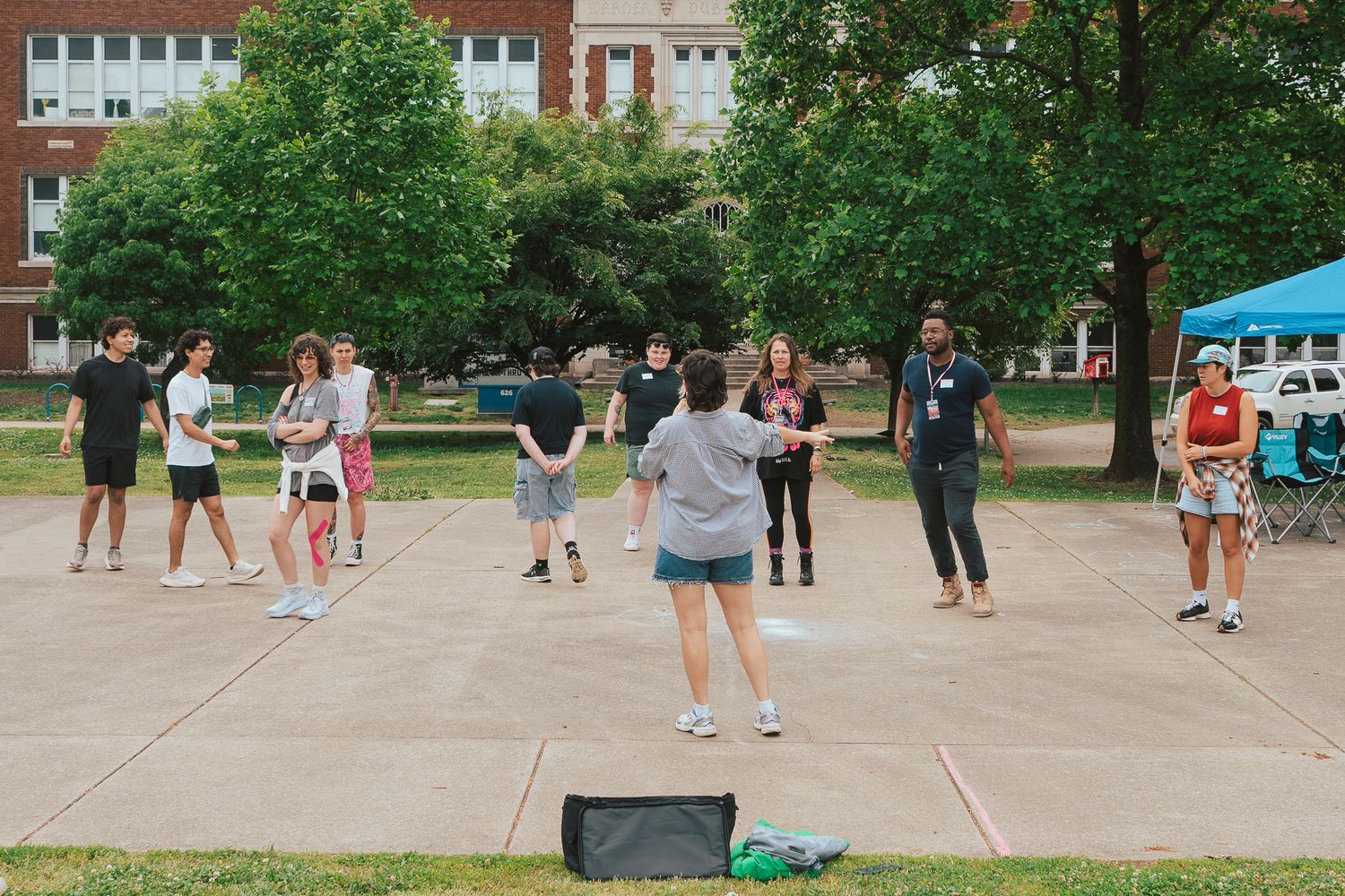 A group of students participates in an outdoor activity on a campus plaza surrounded by trees.
