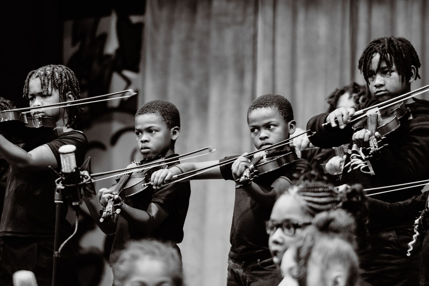 Black and white photo of young children playing violins in a youth orchestra performance.