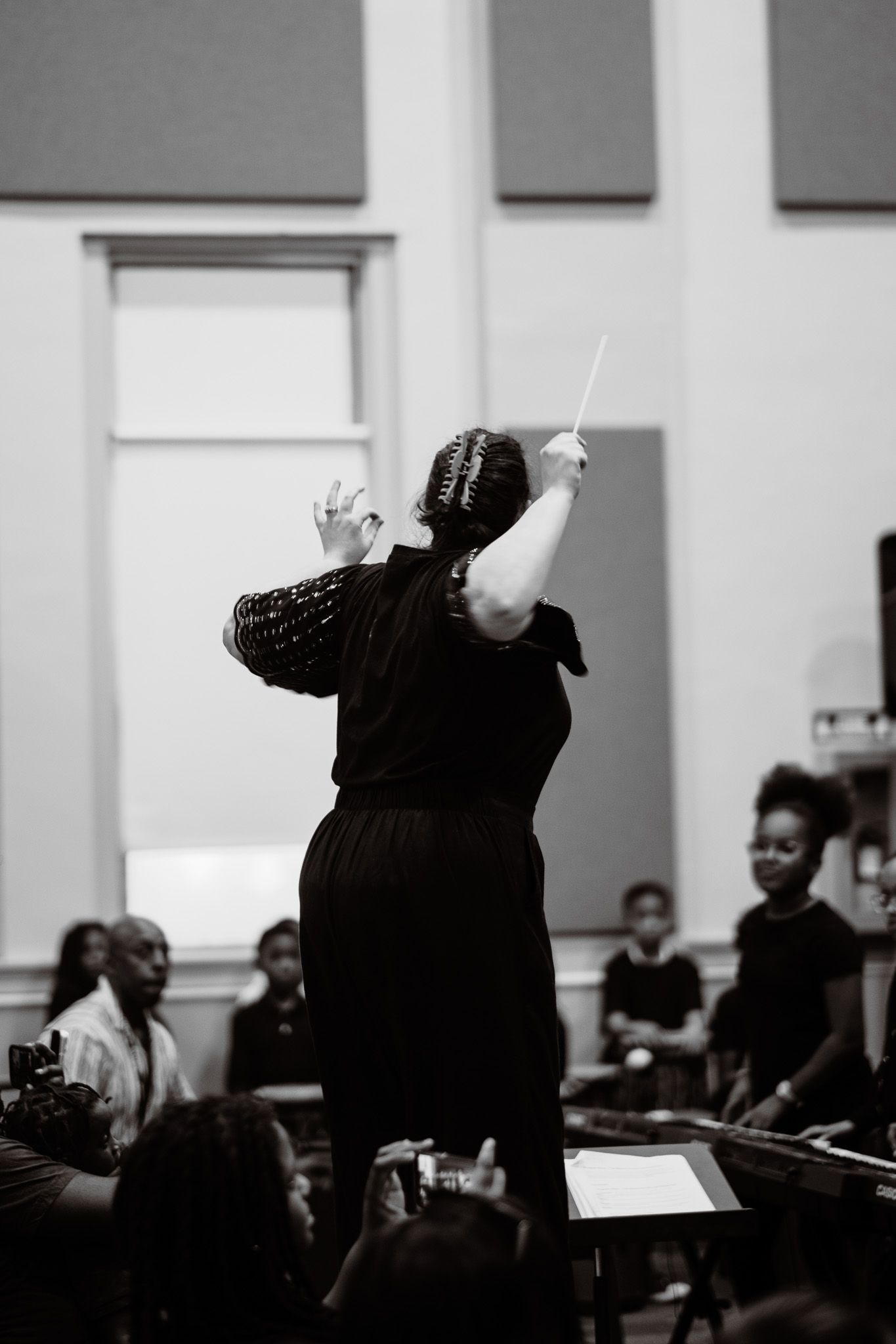 Black and white photo of a female conductor raising her baton before a youth orchestra ensemble.