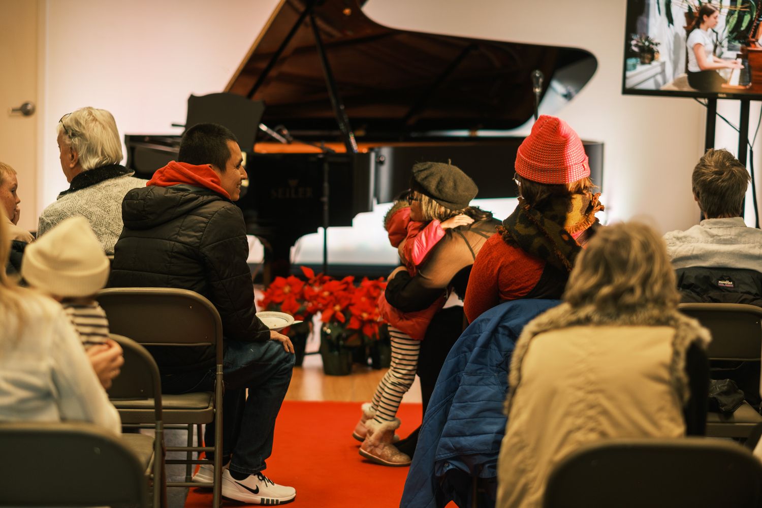Audience members watch a grand piano performance at a holiday recital with red poinsettias decorating the stage.
