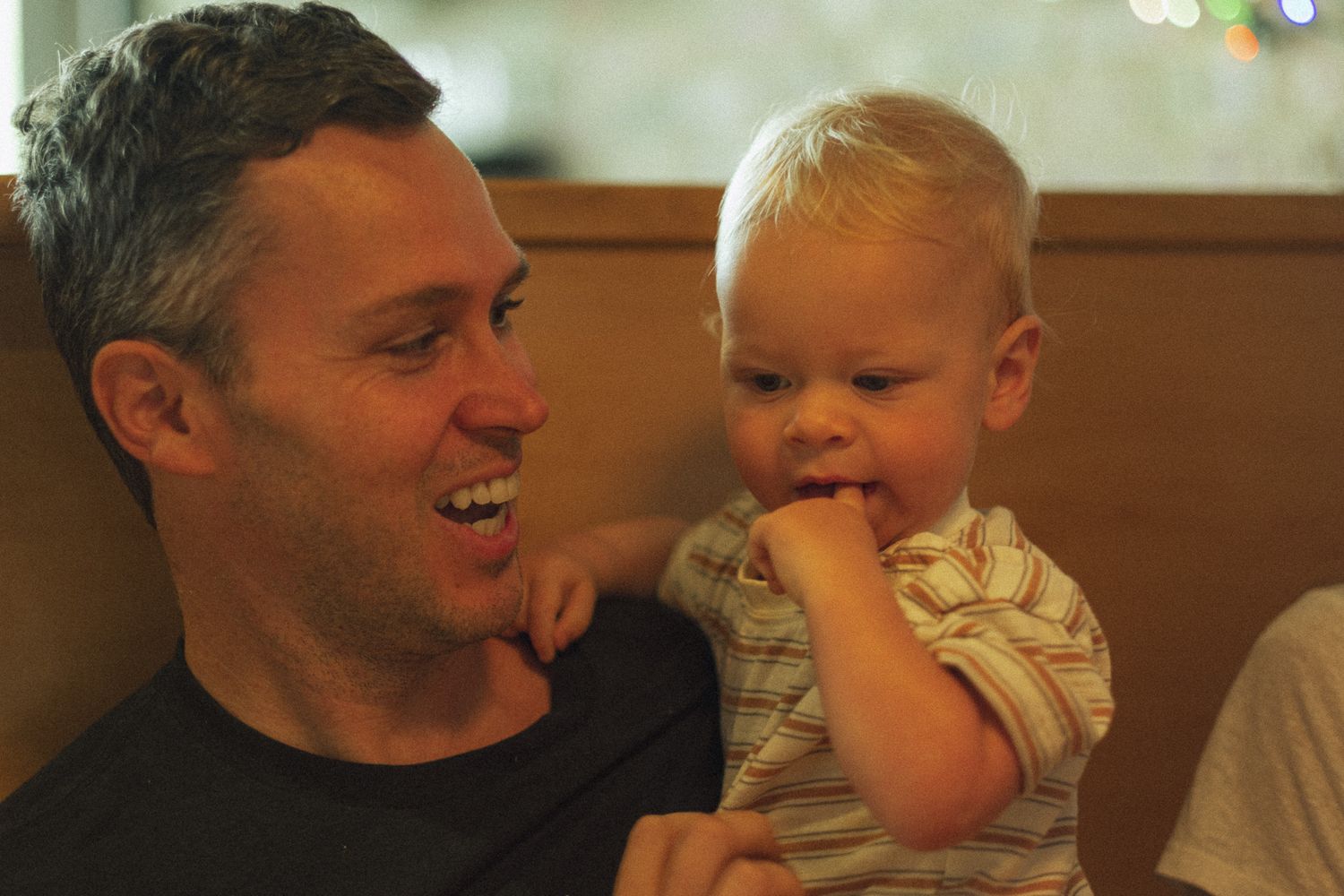 Cheerful father holding his young blonde toddler at a restaurant booth.