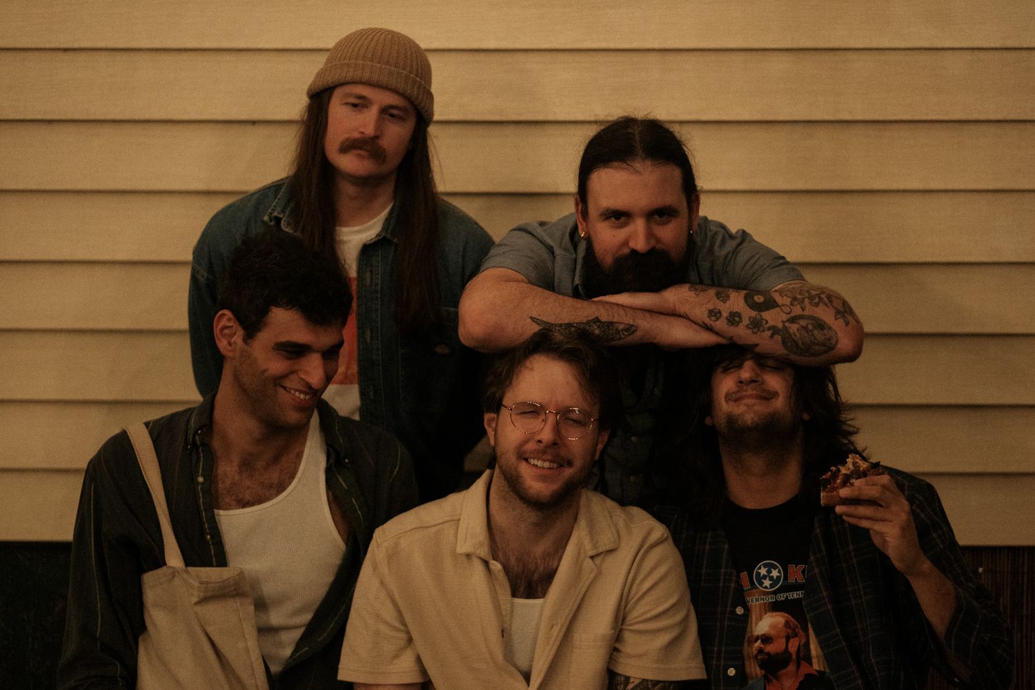 Group portrait of five young men posing casually together outside a building with siding.