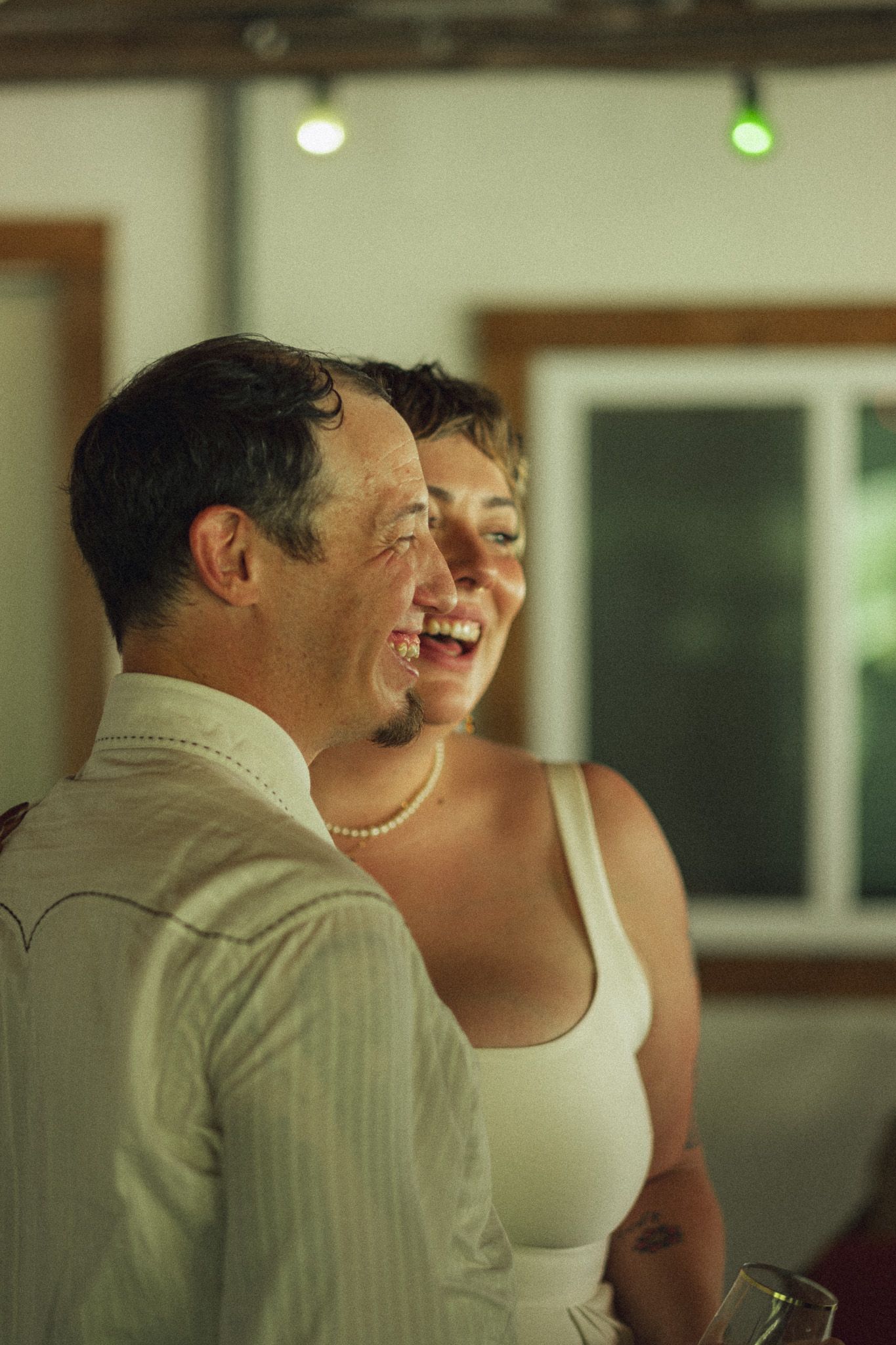 Bride and groom laughing together joyfully at their wedding reception in a warmly lit venue.