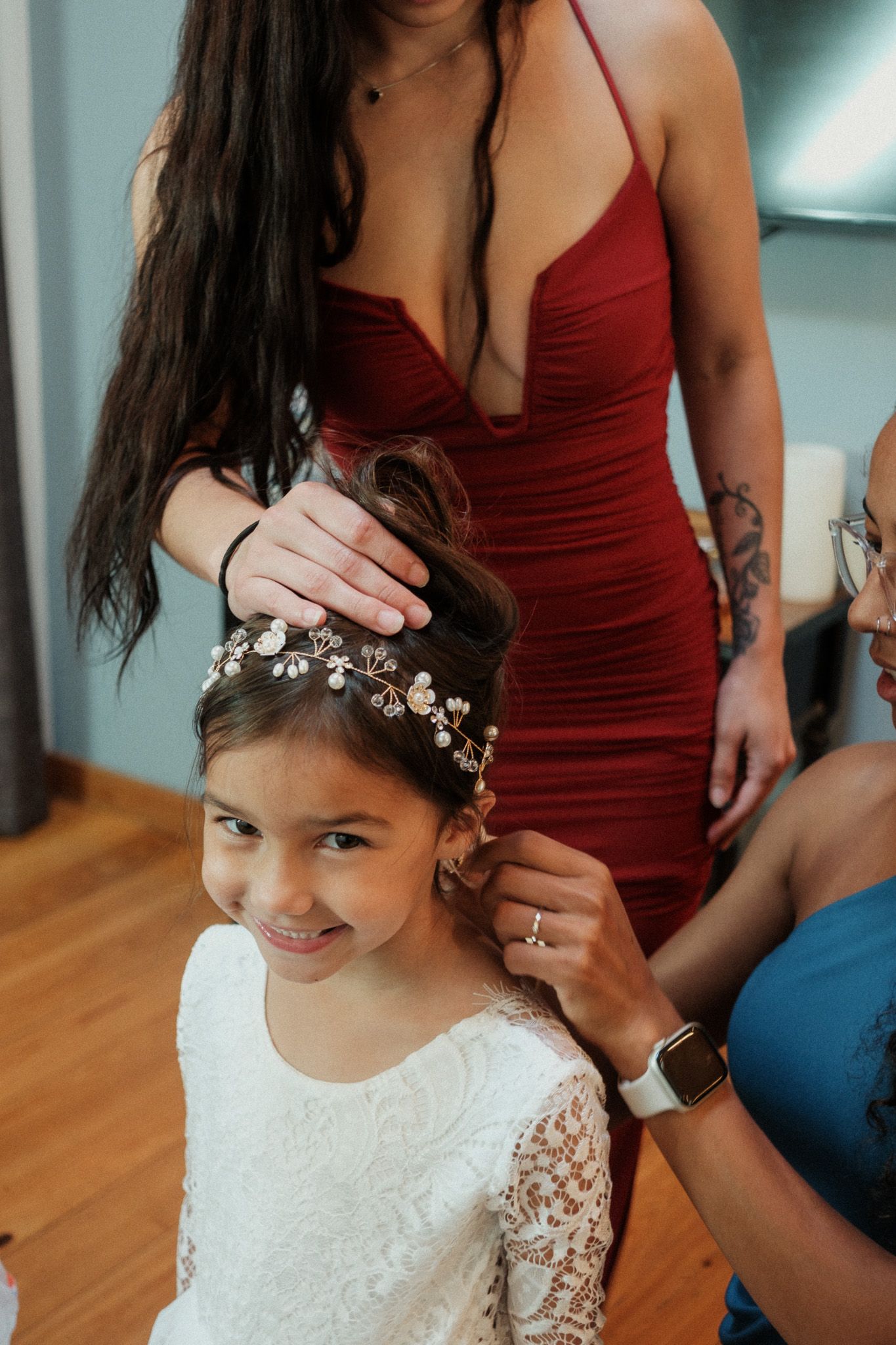Young flower girl smiling as women place a floral crown on her hair before a wedding.