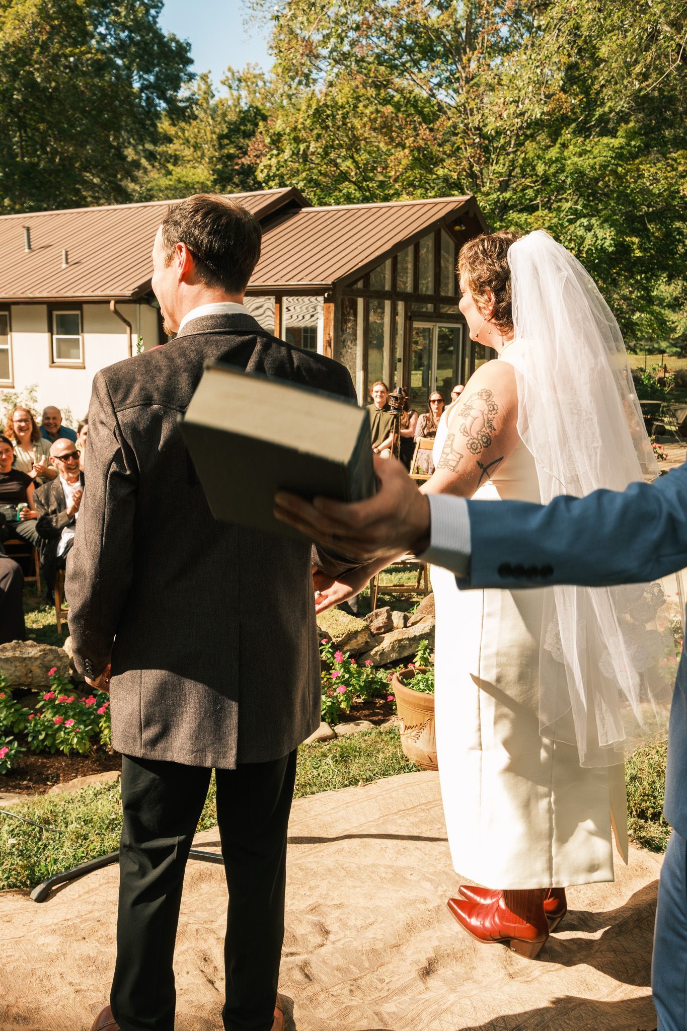 Bride and groom stand at outdoor wedding altar as officiant holds ceremony book for guests.