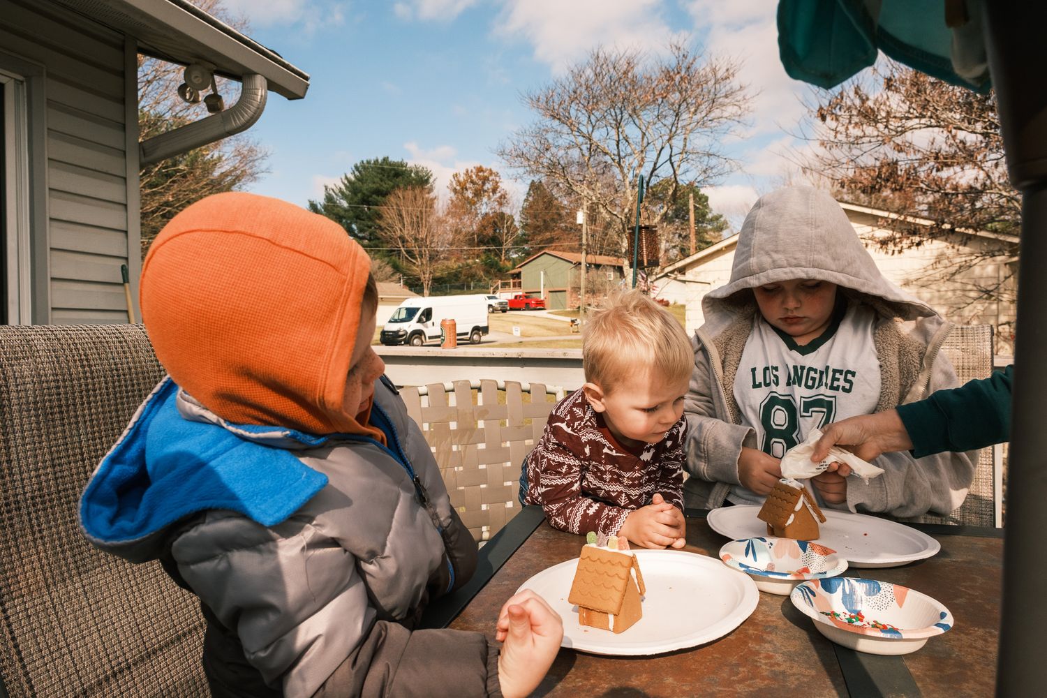 Three young children decorating gingerbread houses at an outdoor table in autumn.