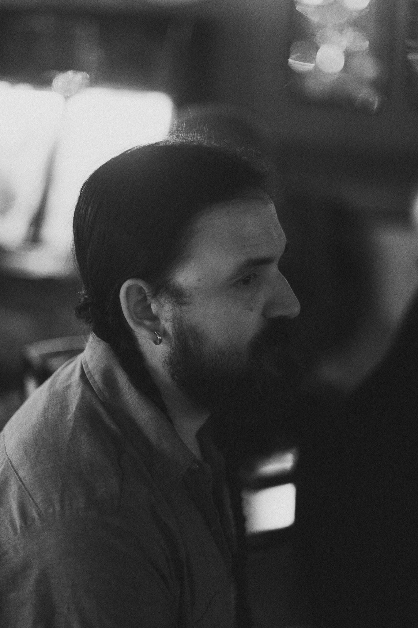 Black and white profile portrait of a bearded man with an earring in a dimly lit indoor setting.