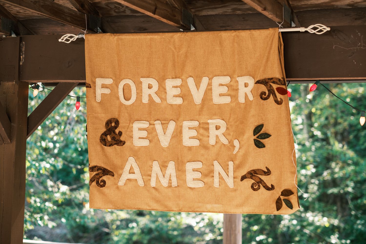 Rustic burlap banner reading Forever and Ever Amen hanging at outdoor wedding ceremony venue.