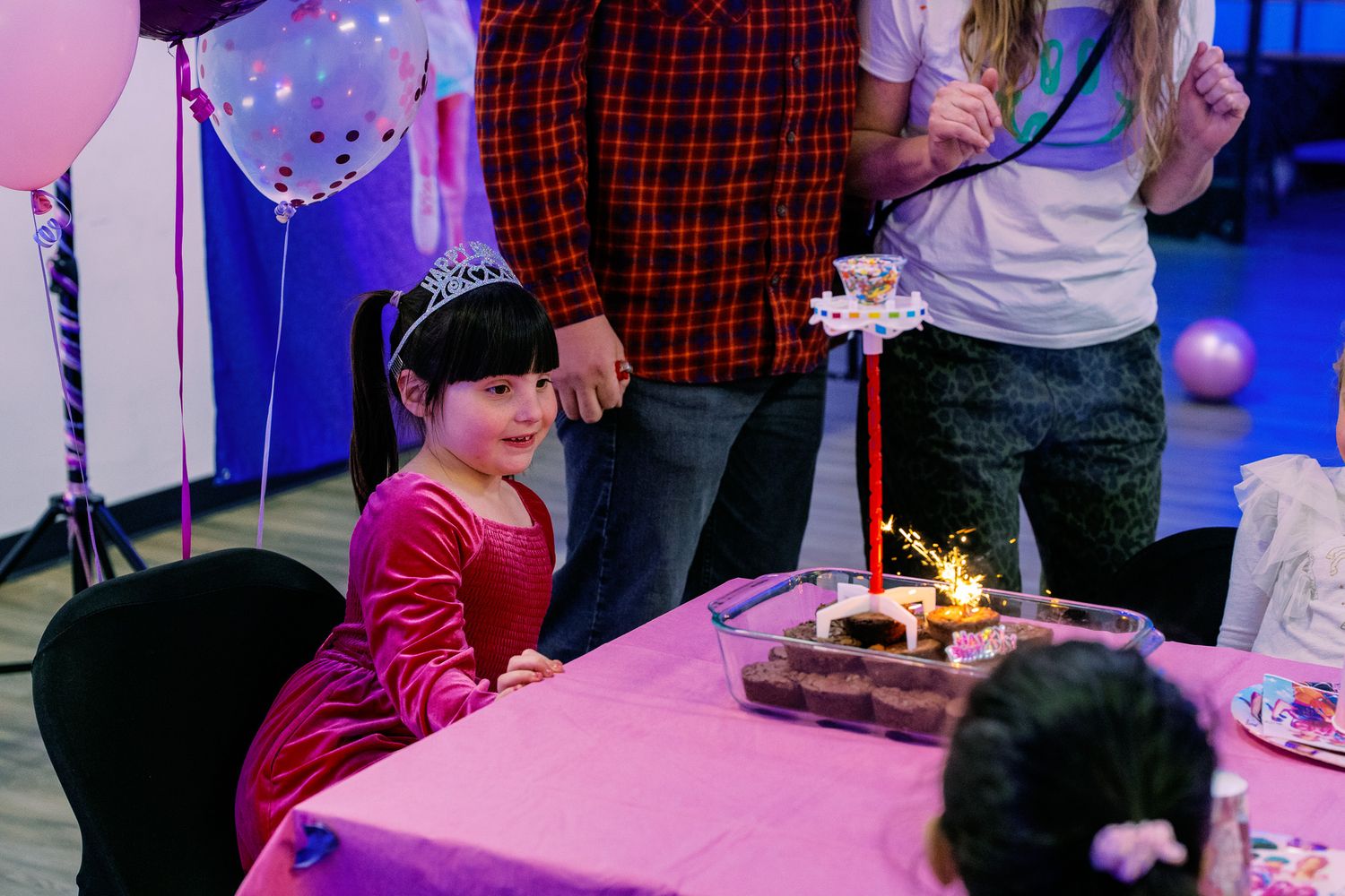 Young girl in a princess dress celebrating her birthday with a sparkler cake at a party.