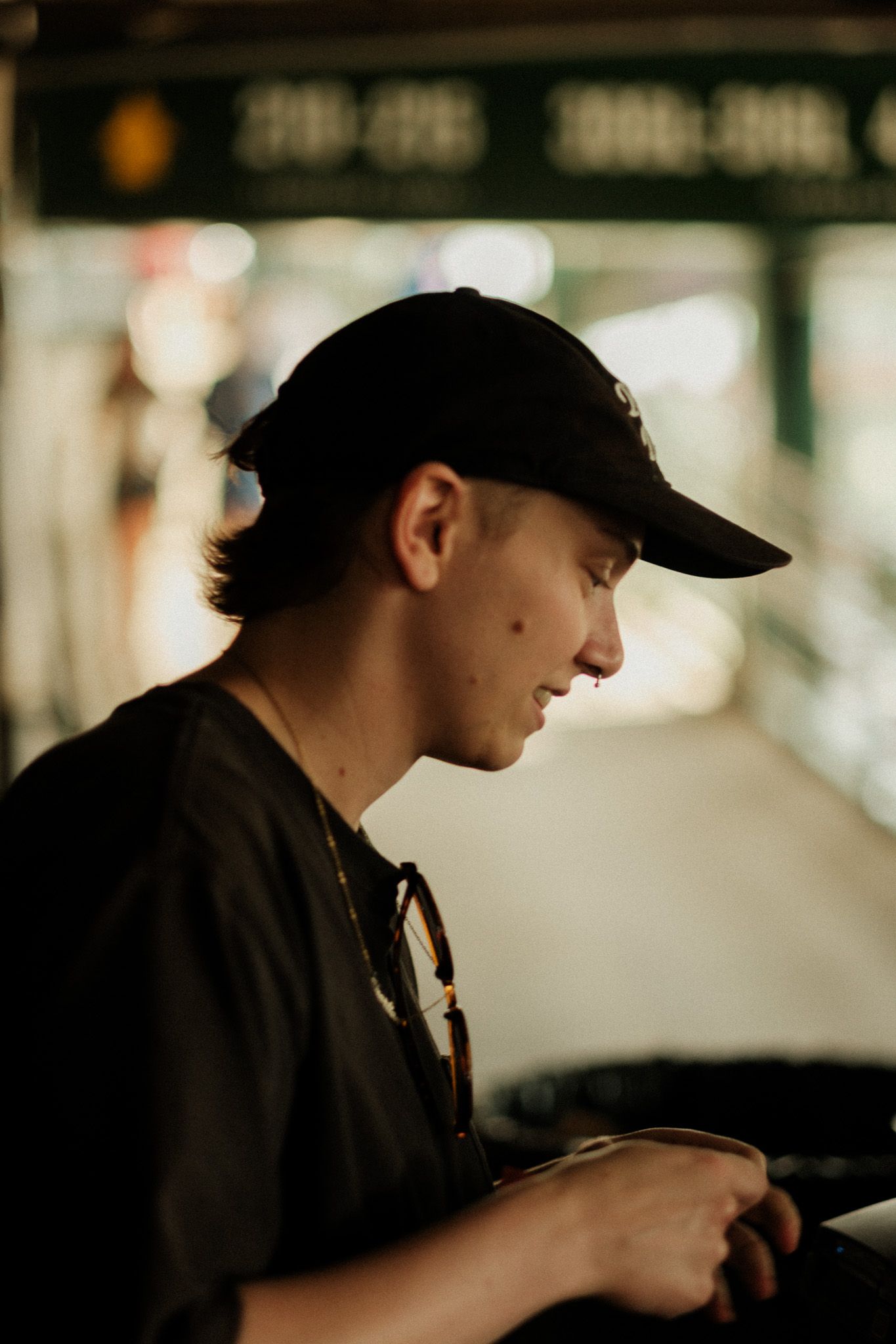 Side profile of a young man in a black cap looking down at something in his hands at a transit station.