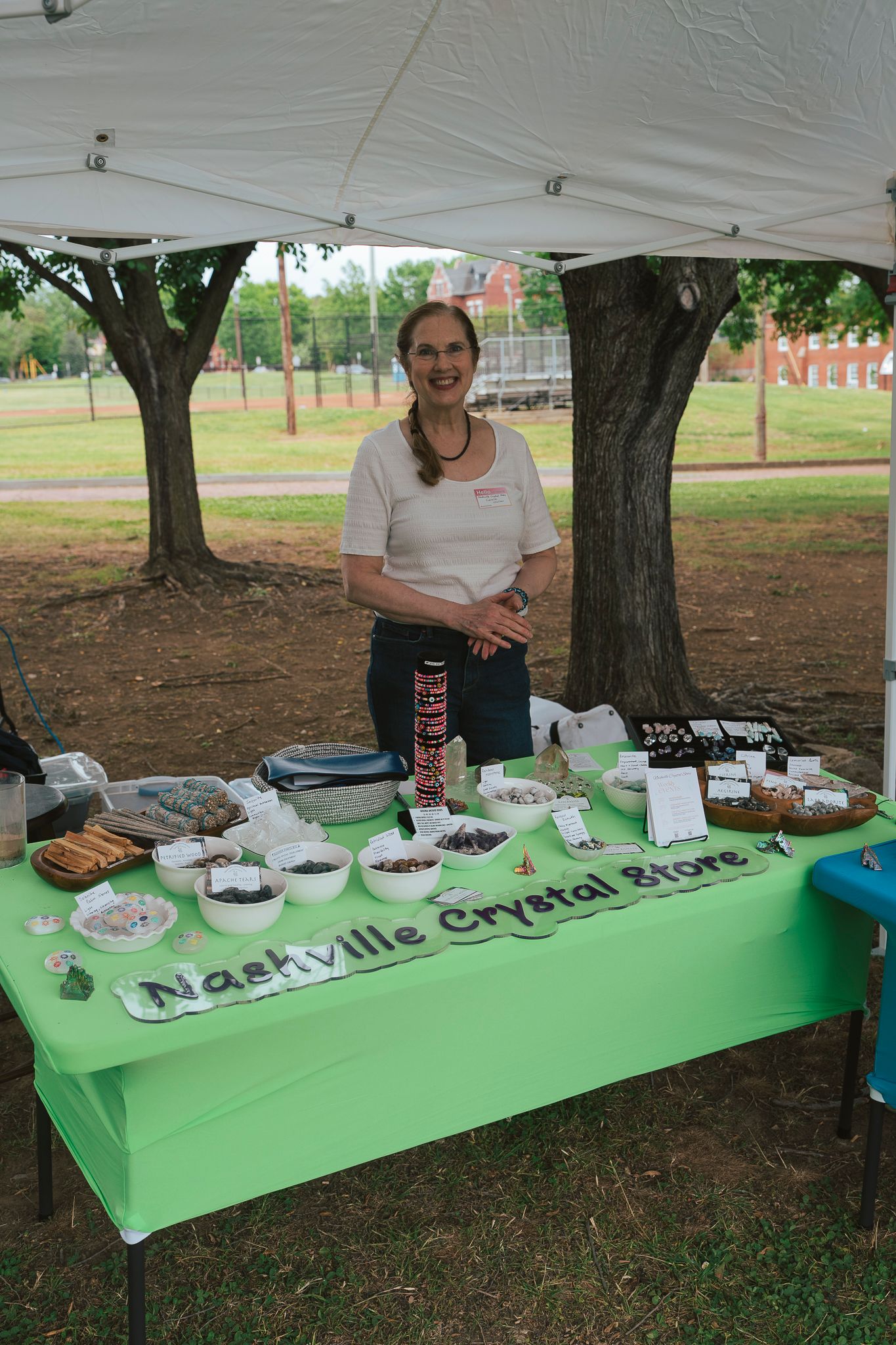 Woman smiling behind Nashville Crystal Store display table with crystals and minerals outdoors.