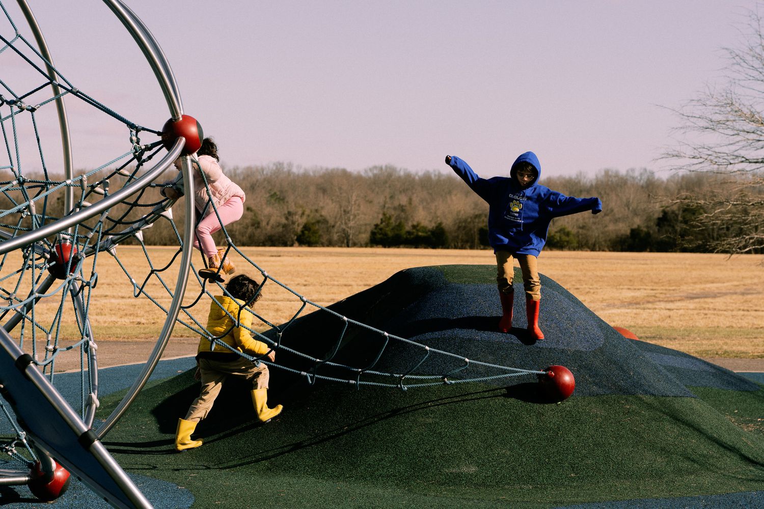 Three children playing on an outdoor playground climbing structure on a clear winter day.