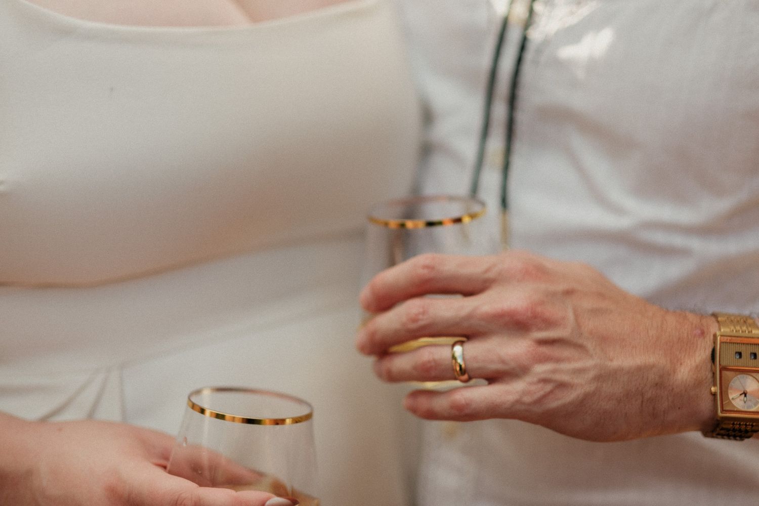 Close-up of couple holding gold-rimmed champagne flutes at wedding celebration.