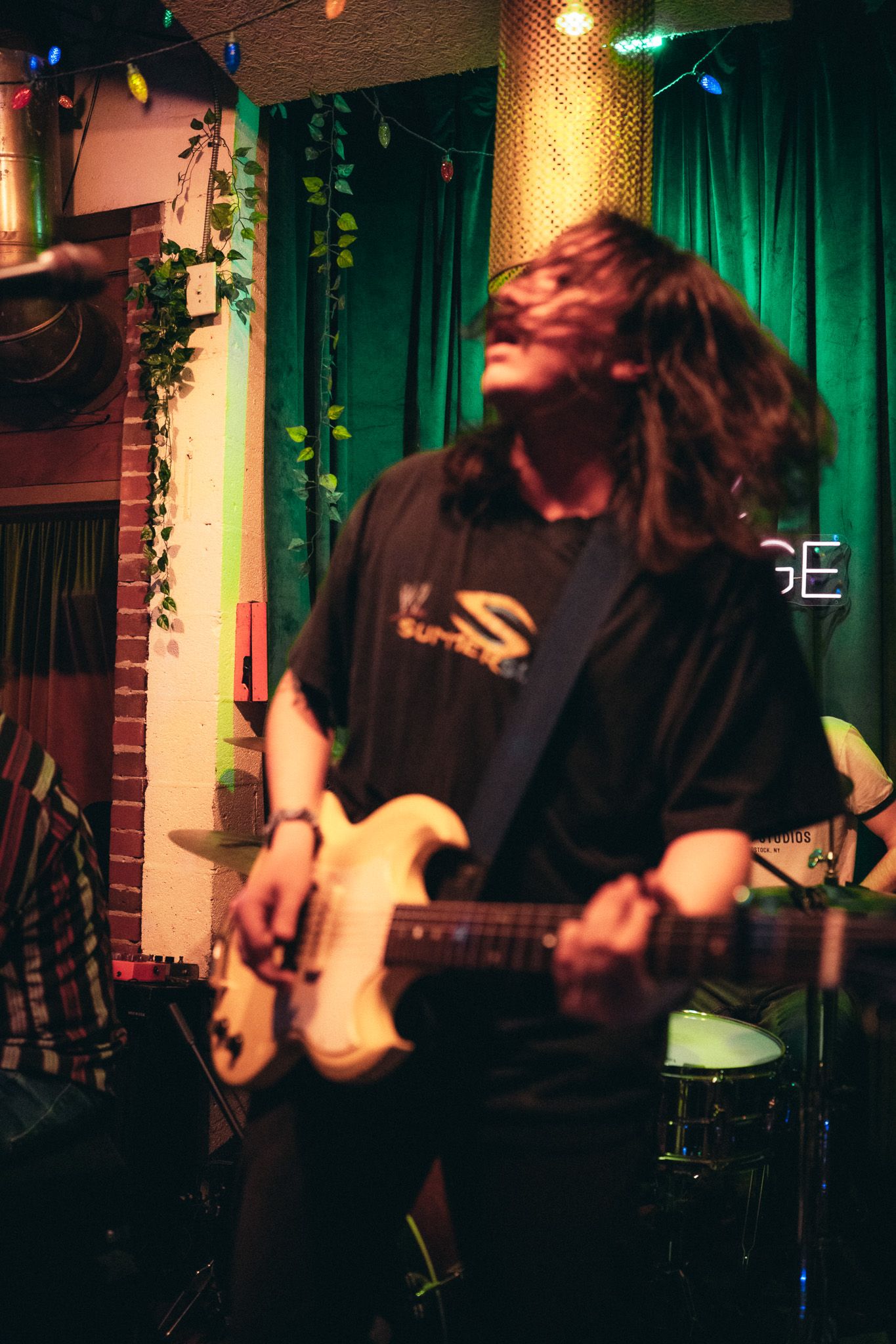 Long-haired guitarist in Surge t-shirt headbanging while playing electric guitar on stage.