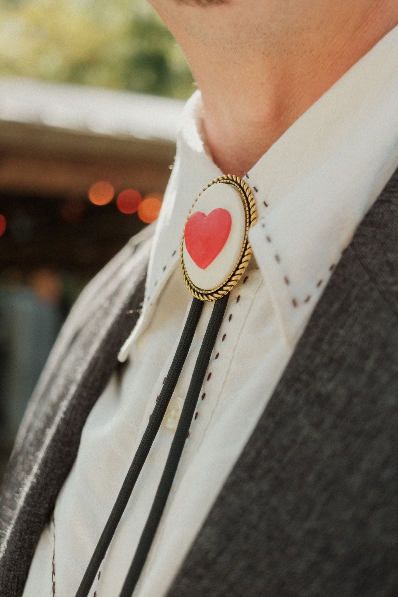 Close-up of groom's bolo tie featuring red heart pendant on white western shirt with dark blazer.
