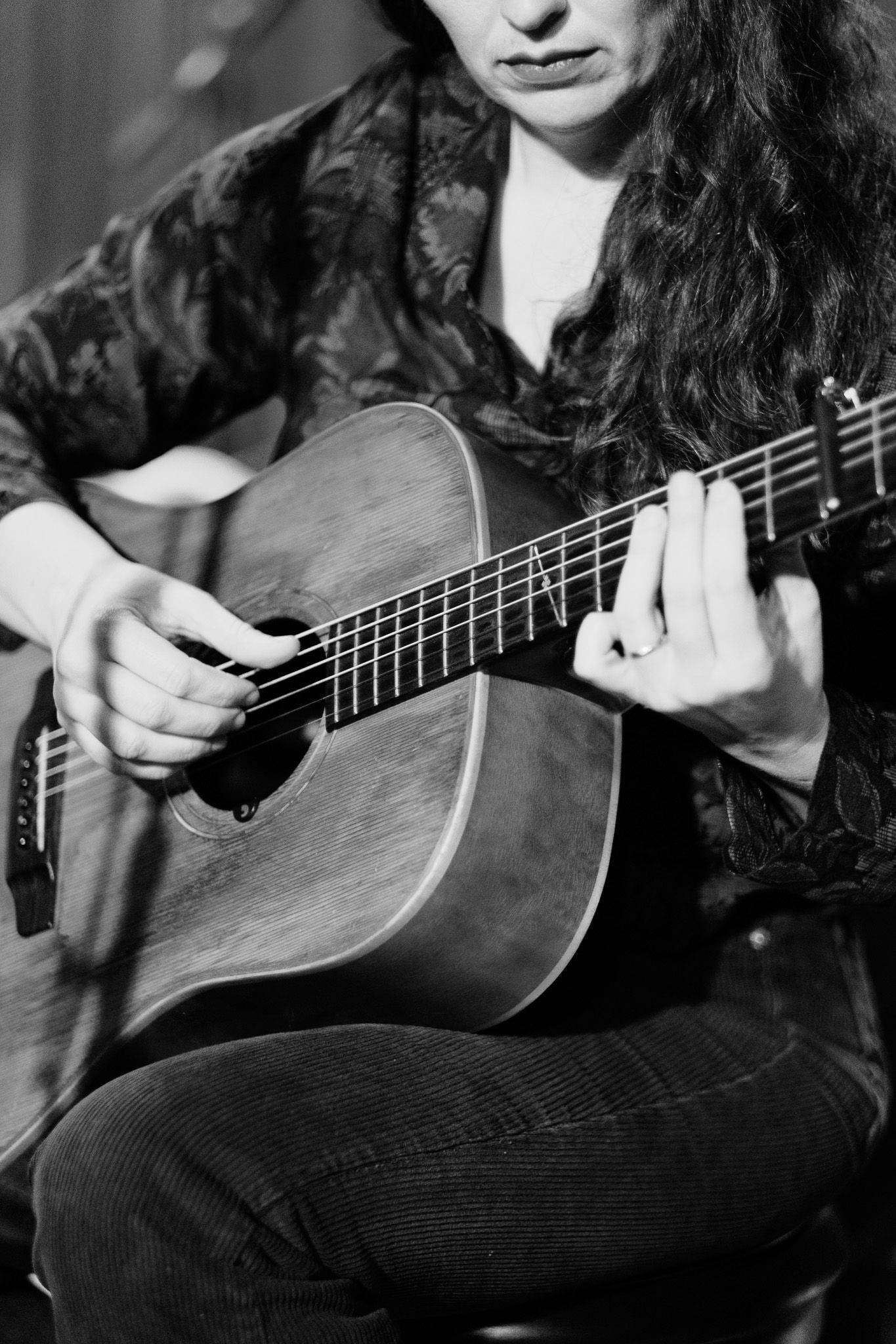 Black and white close-up of a curly-haired woman playing an acoustic guitar while seated.