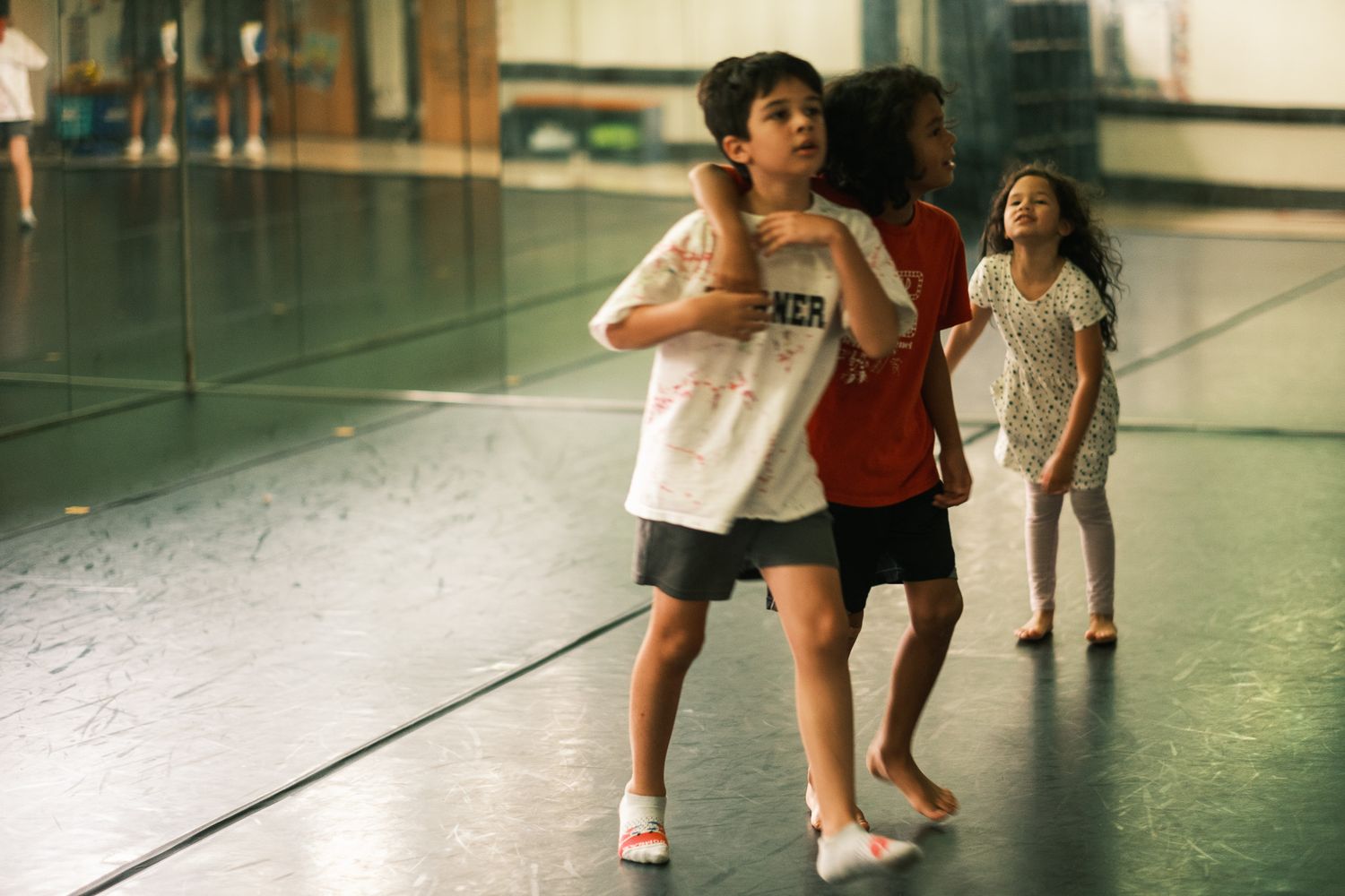 Children practicing dance moves together in a mirrored dance studio.