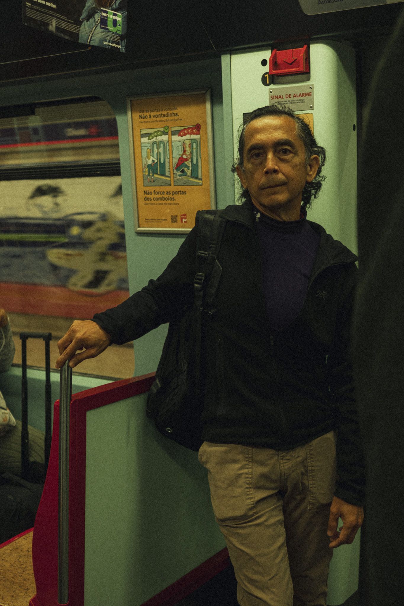 Middle-aged man with a backpack standing inside a subway train holding a handrail.