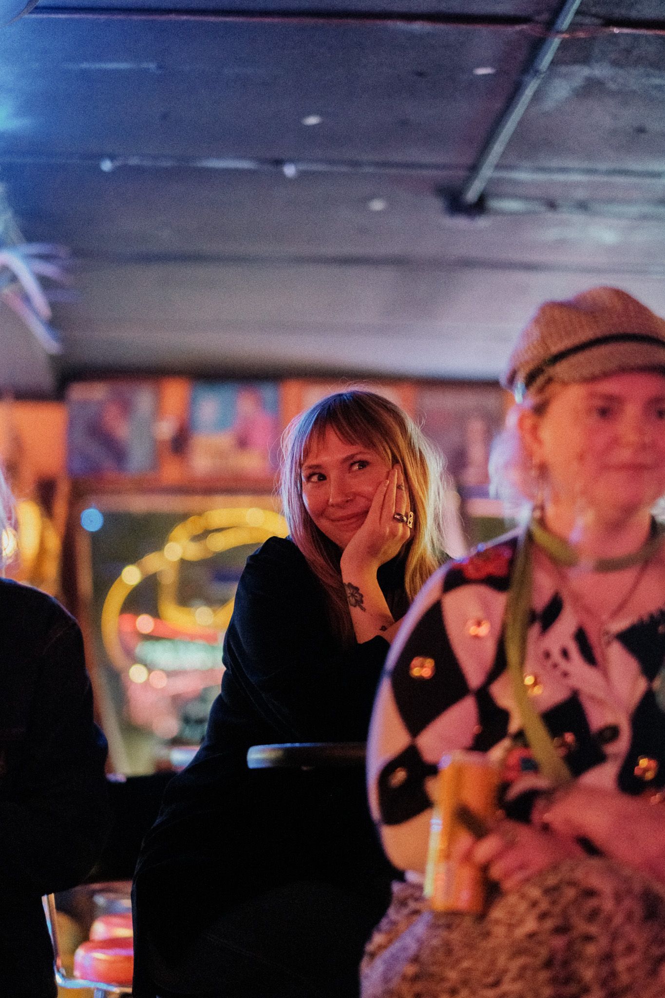 Young woman with blonde hair smiles warmly in a cozy, warmly lit bar setting.
