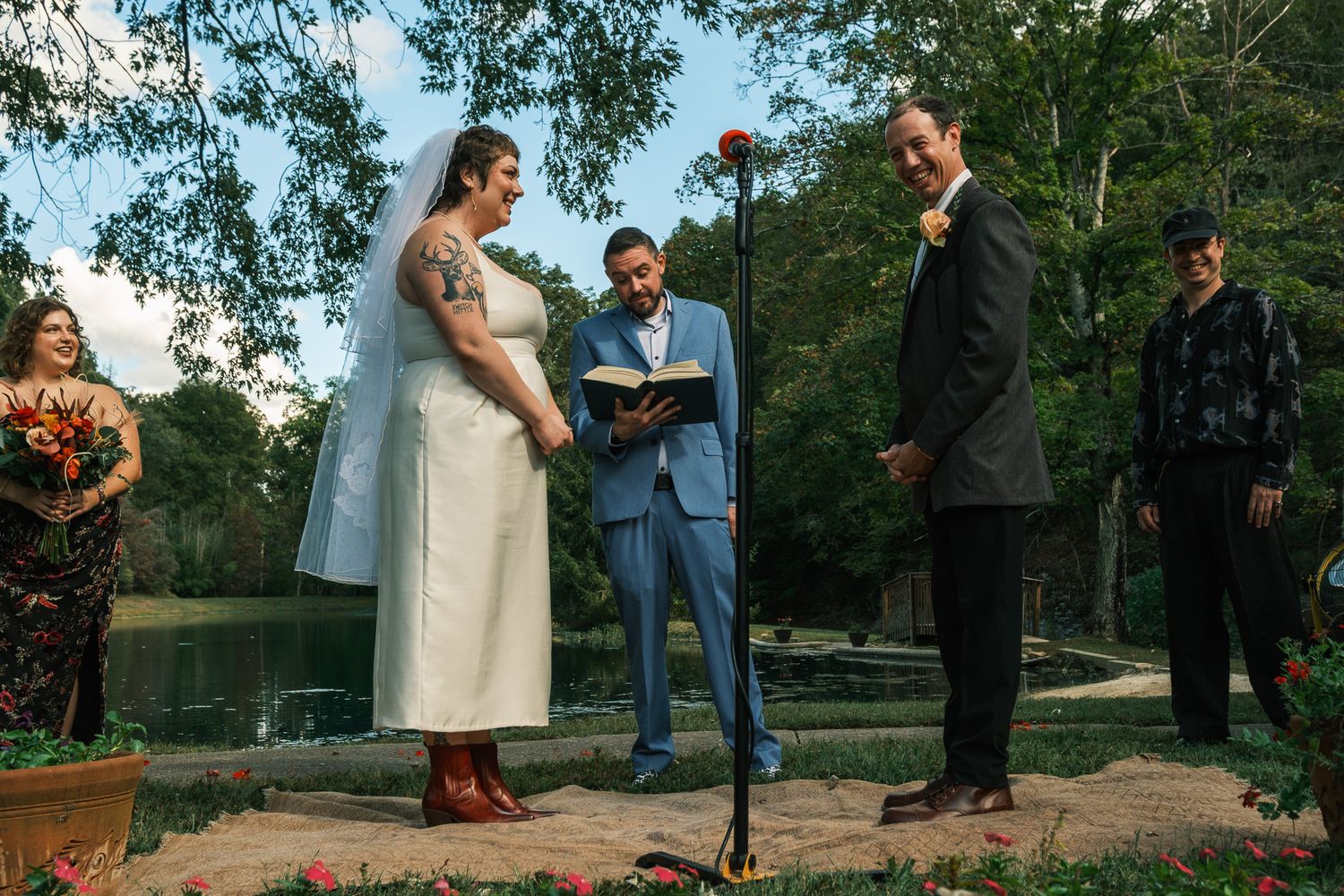 Bride and groom exchange vows at outdoor waterfront ceremony with officiant and wedding party.