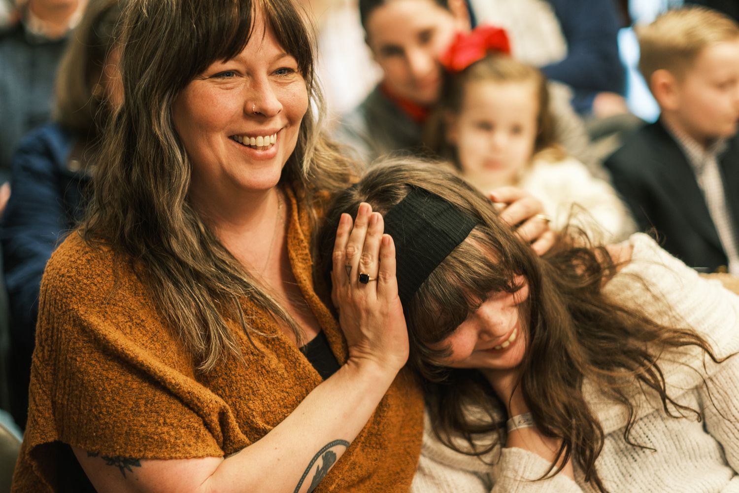 Woman with tattooed hands laughs while tenderly touching another woman's hair at joyful gathering.