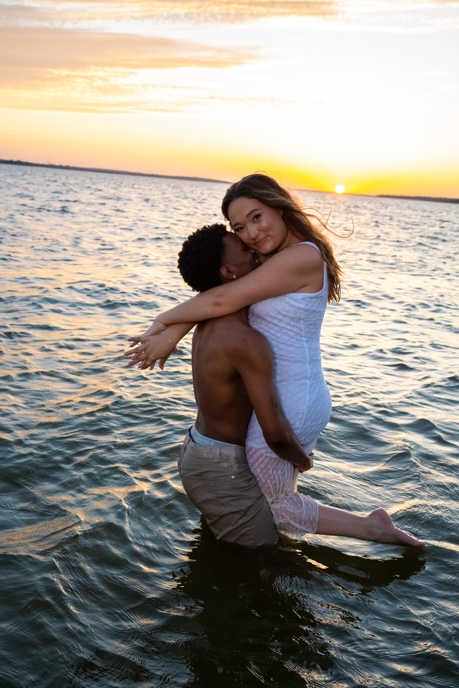 A couple embraces in the ocean water during a romantic sunset photoshoot with golden light reflecting on the waves shot by Kin & Lens