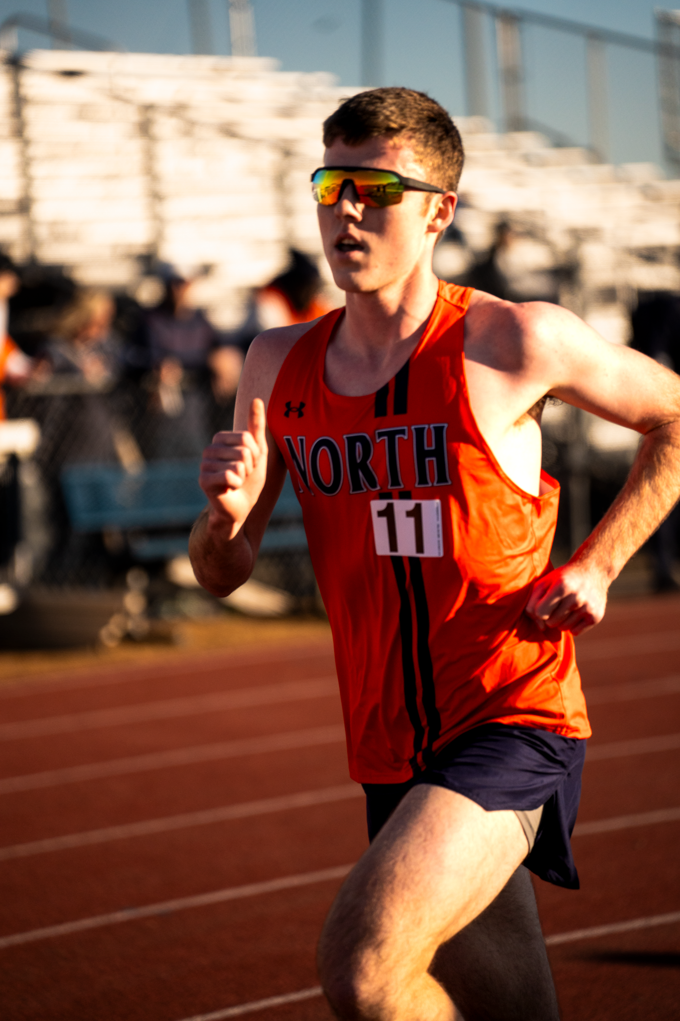 Track athlete in orange jersey running on an outdoor track during competition.