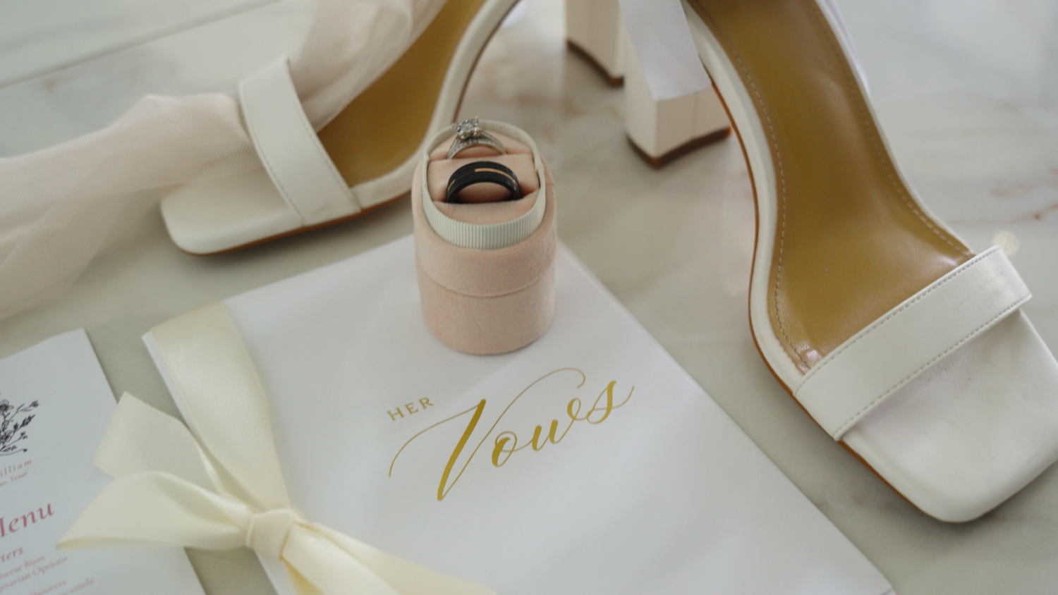 White bridal heels and wedding accessories arranged on a light beige surface for a romantic styling photoshoot by Kin & Lens Creative Media