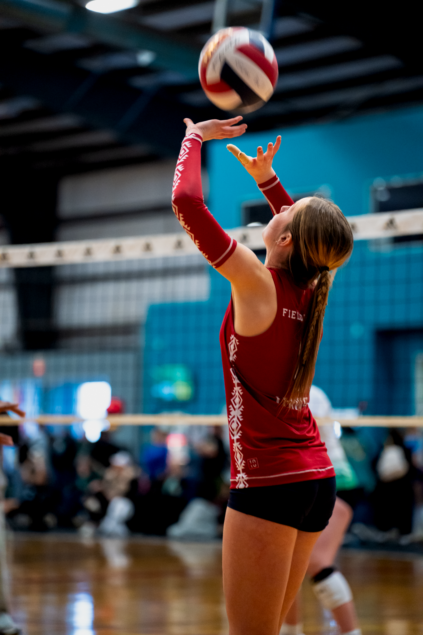 Volleyball player in red jersey serving ball in DFW, TX indoor sports facility by Kin & Lens Creative Media