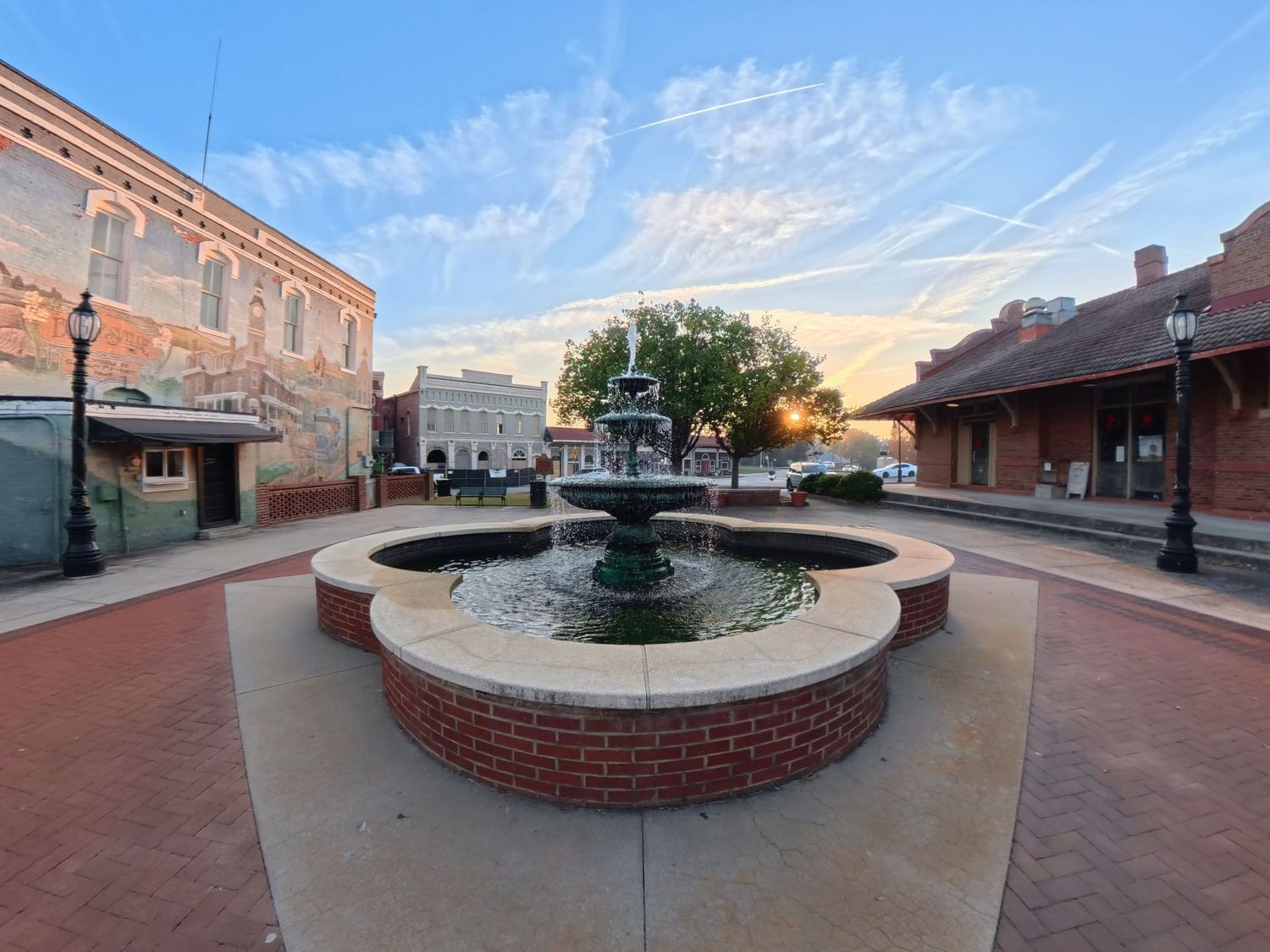 A brick fountain sits in the center of a historic downtown plaza at sunset with historic buildings in the background.