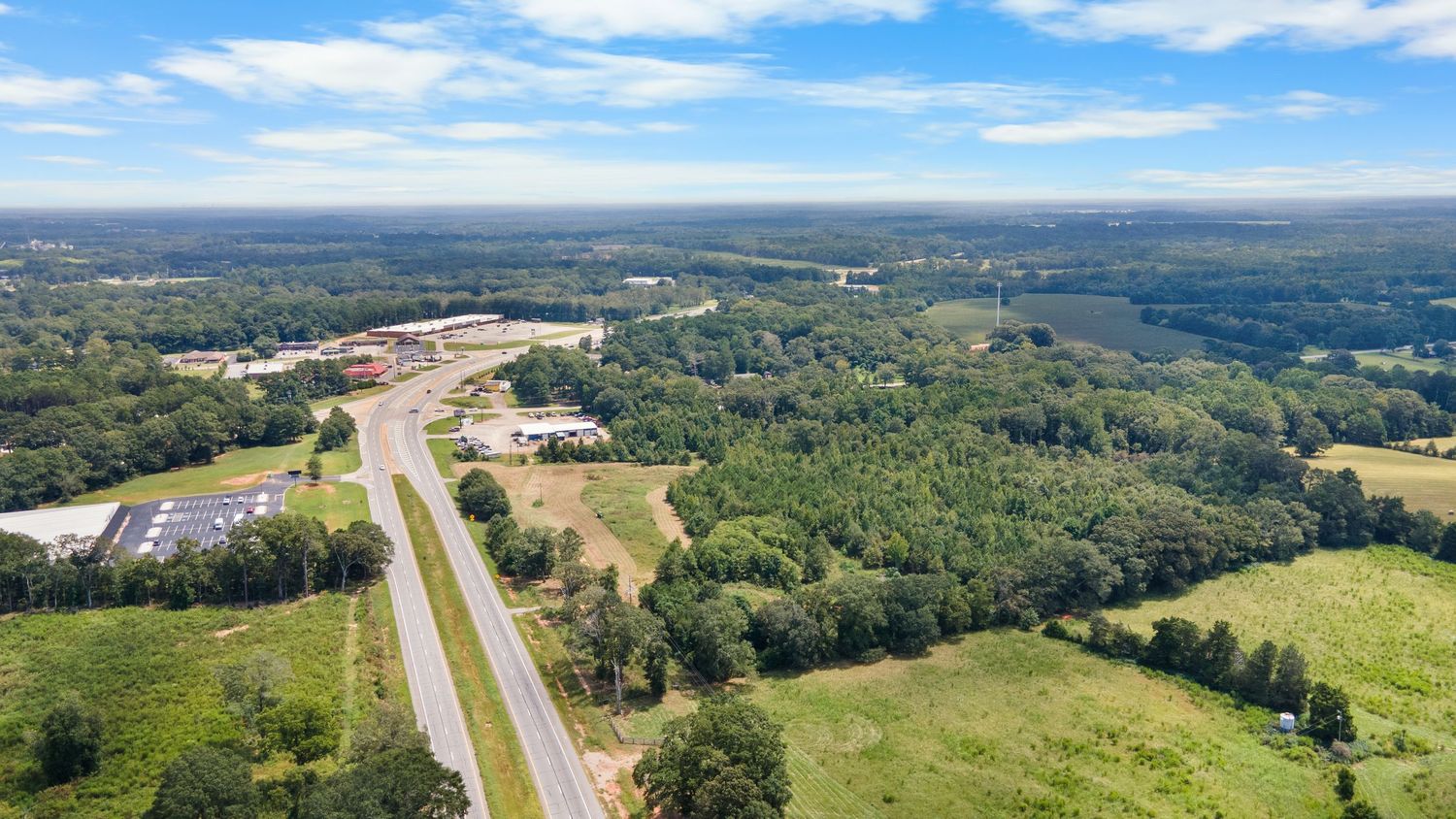 Aerial panoramic view of a divided highway cutting through green rural landscape under blue skies with white clouds.
