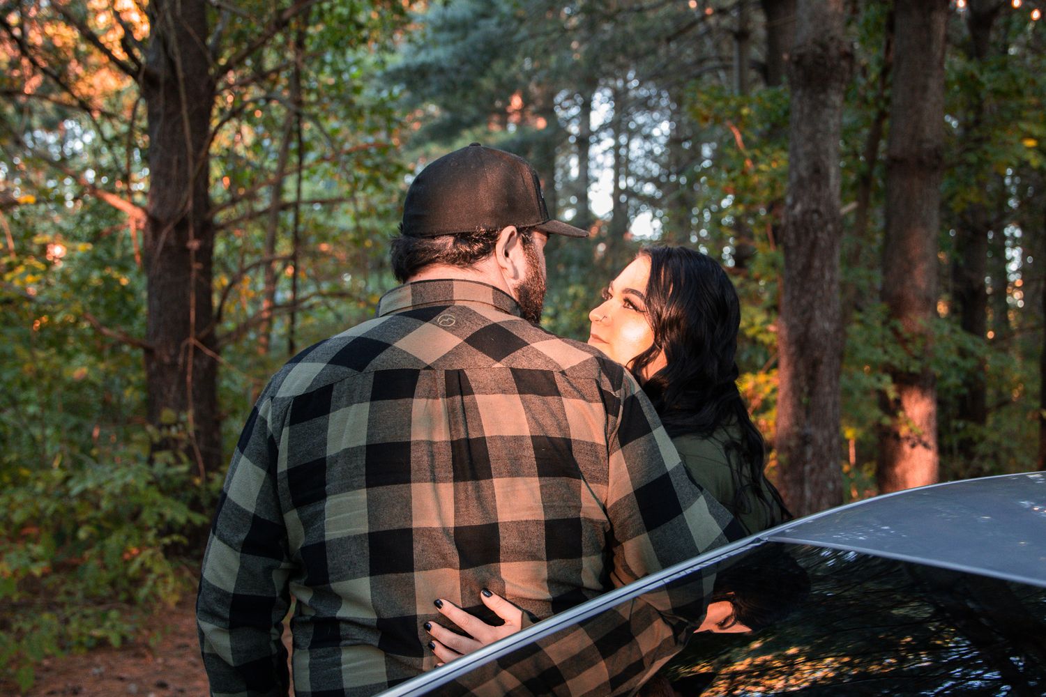 Two people in plaid shirts embrace in a romantic moment among autumn trees during golden hour.