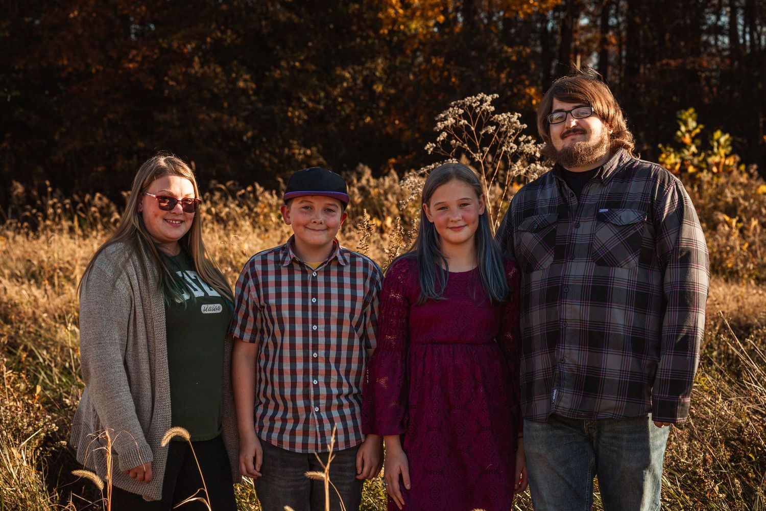 A fall family portrait with four people wearing plaid and casual attire in an autumn field.