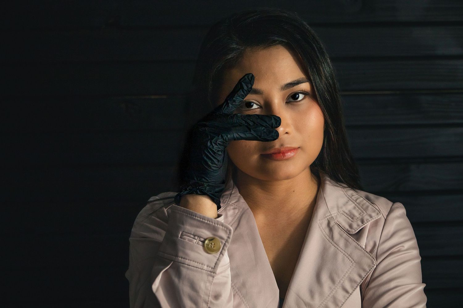 Young woman in white jacket wearing black glove, posing dramatically against dark wooden background.