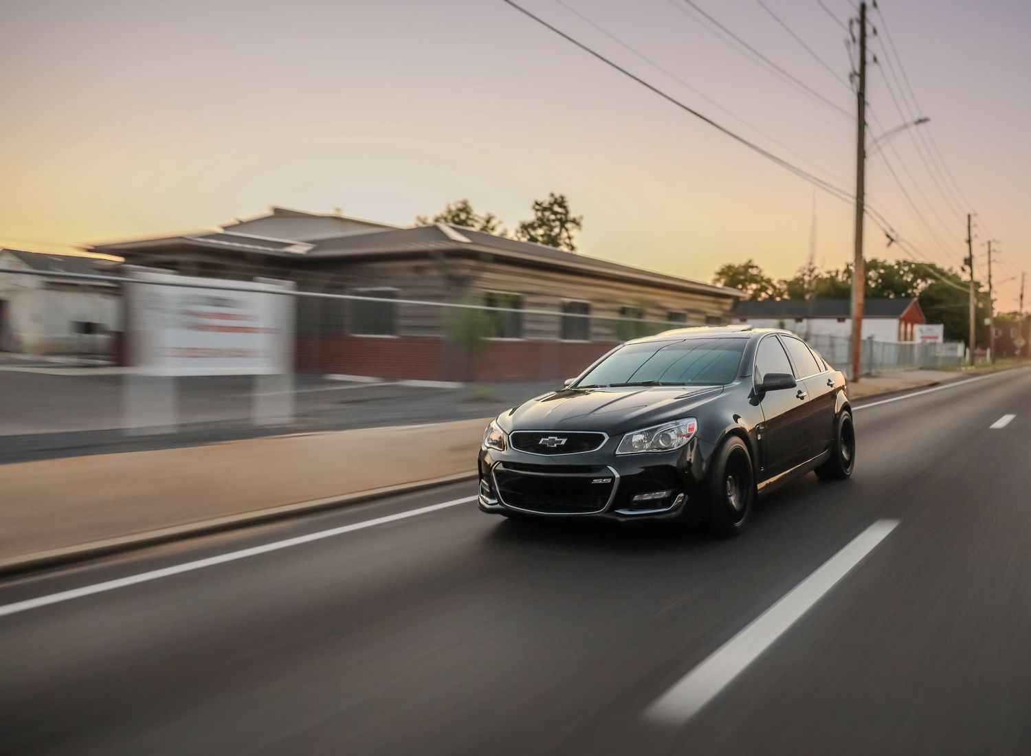Black sports car driving on an empty road at dusk.
