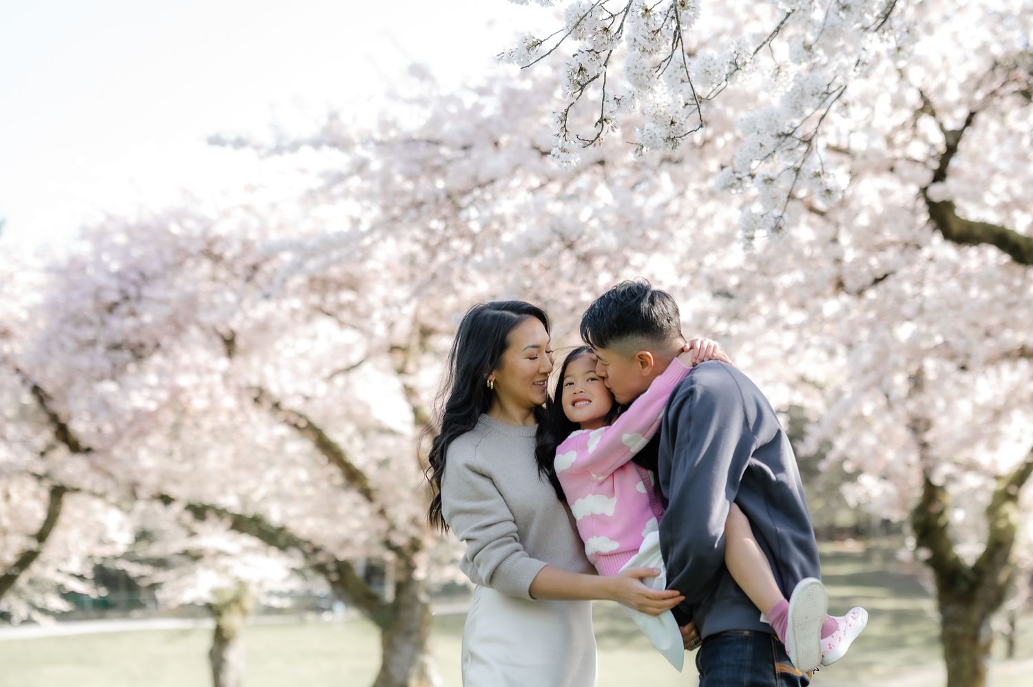 Happy family enjoying springtime under blooming cherry blossom trees in a park.