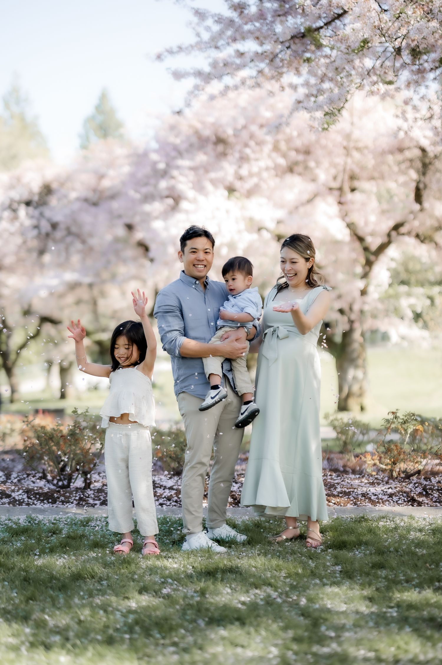 A family poses together under blooming cherry blossom trees in a spring garden setting.