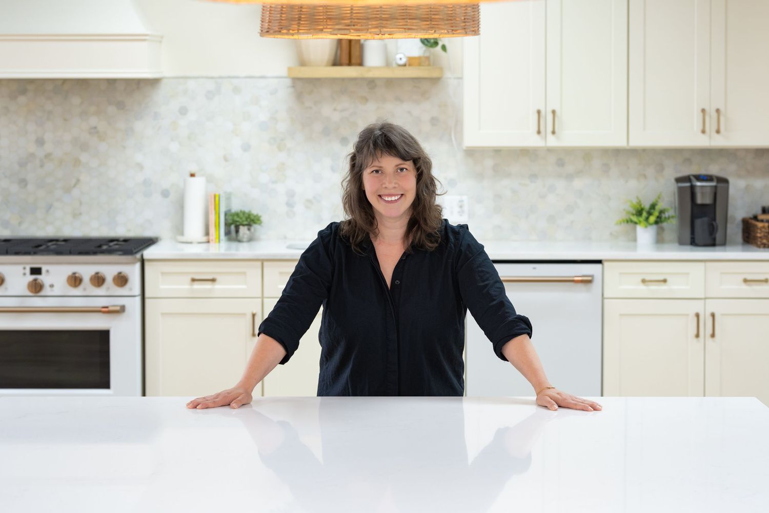 Professional standing in modern white kitchen with marble countertops and wood accents.