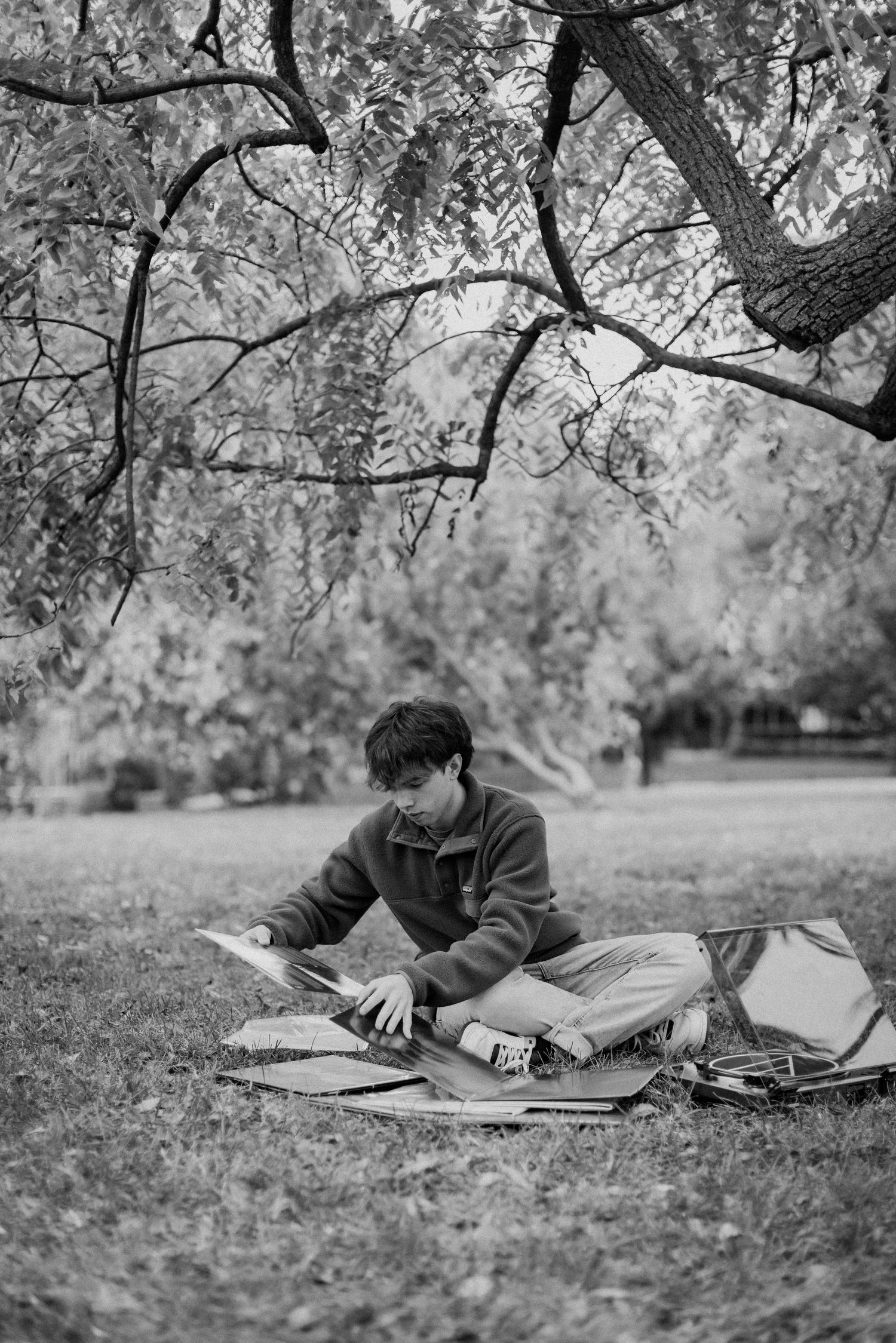 A young man puts an album on his record player with his vinyl collection on the ground around him during a Loose Park senior photo session.