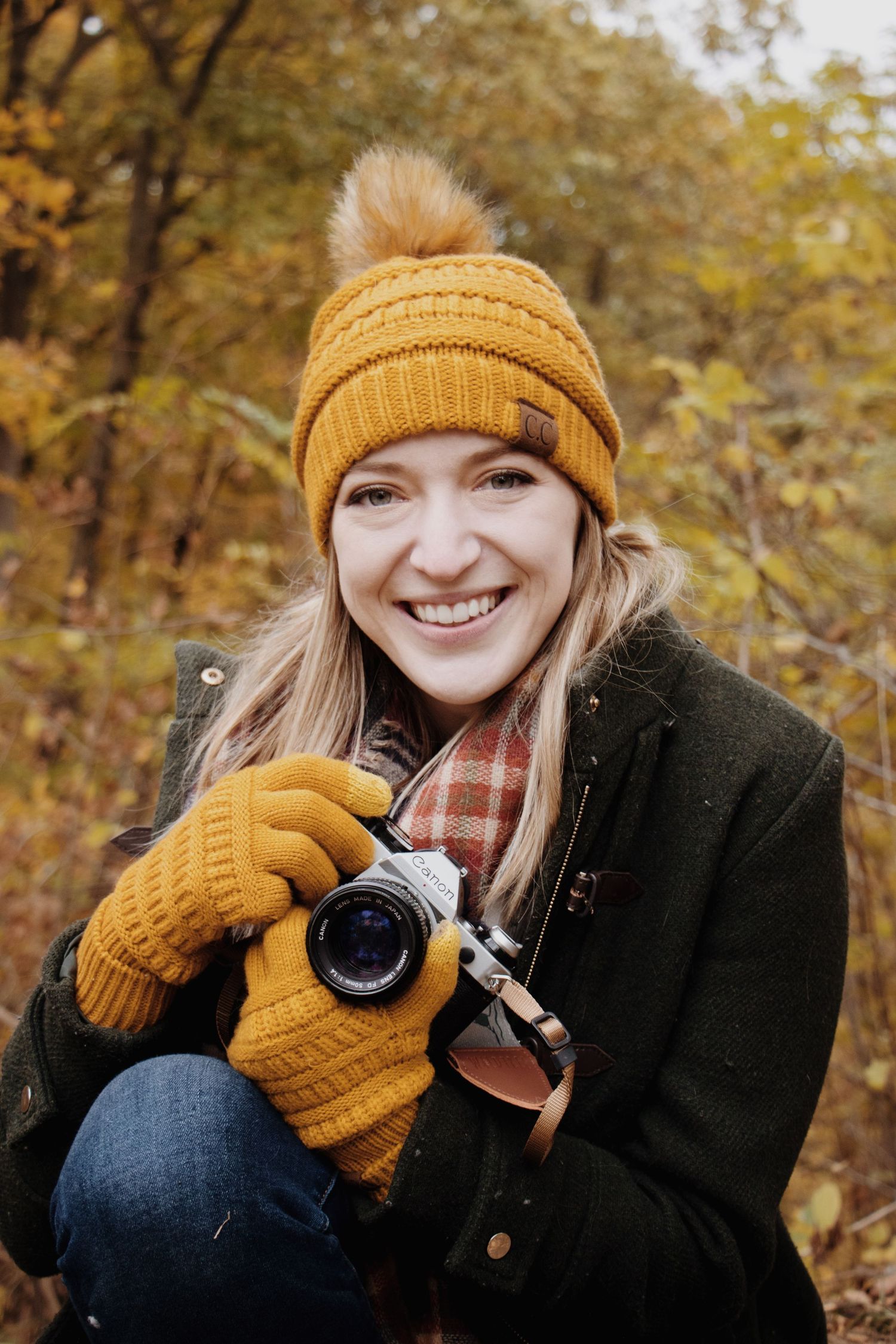 A Kansas City photographer wearing a green coat and mustard yellow gloves and hat smiles while holding a film camera.