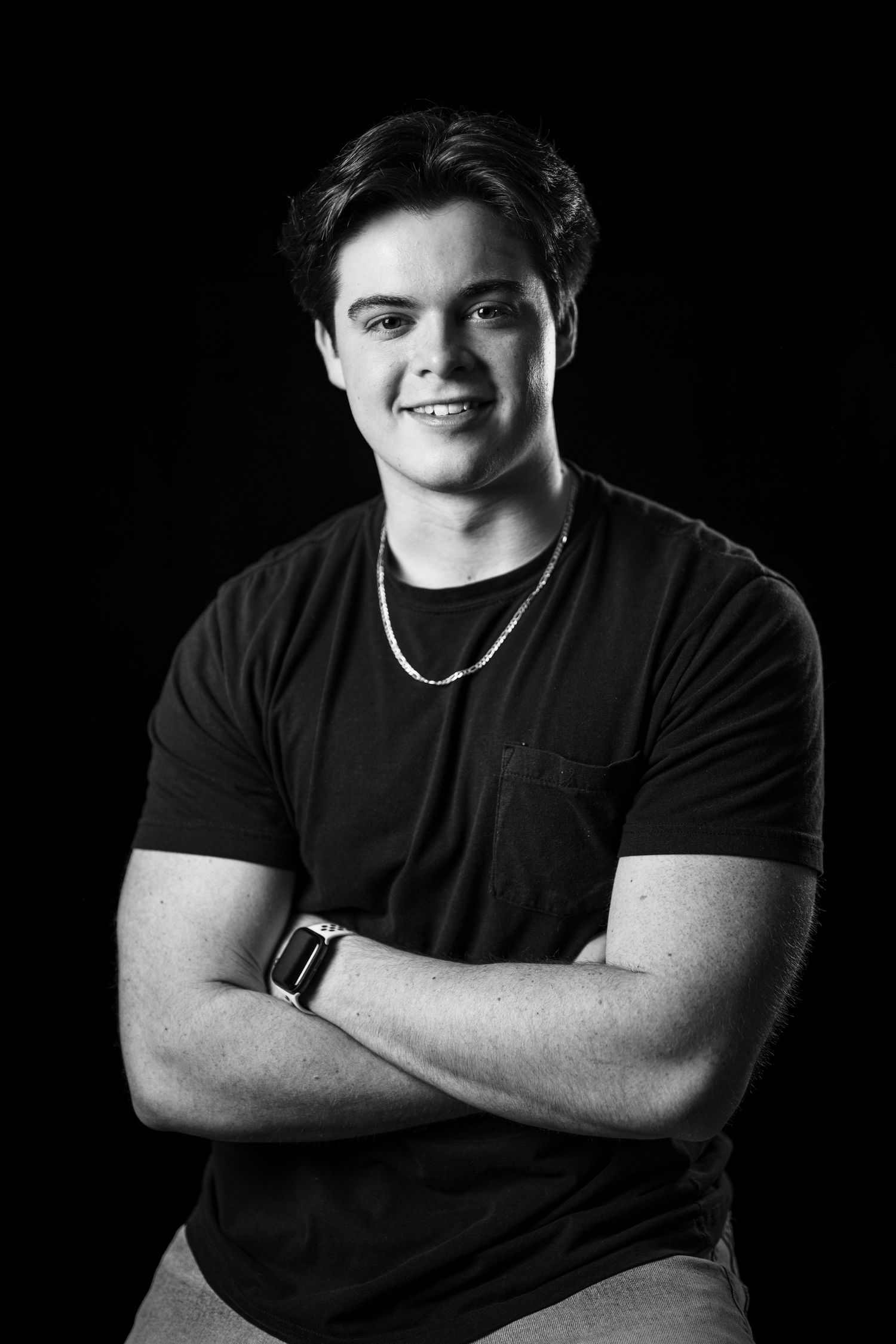 Black and white portrait of a young man smiling with arms crossed wearing a black t-shirt.