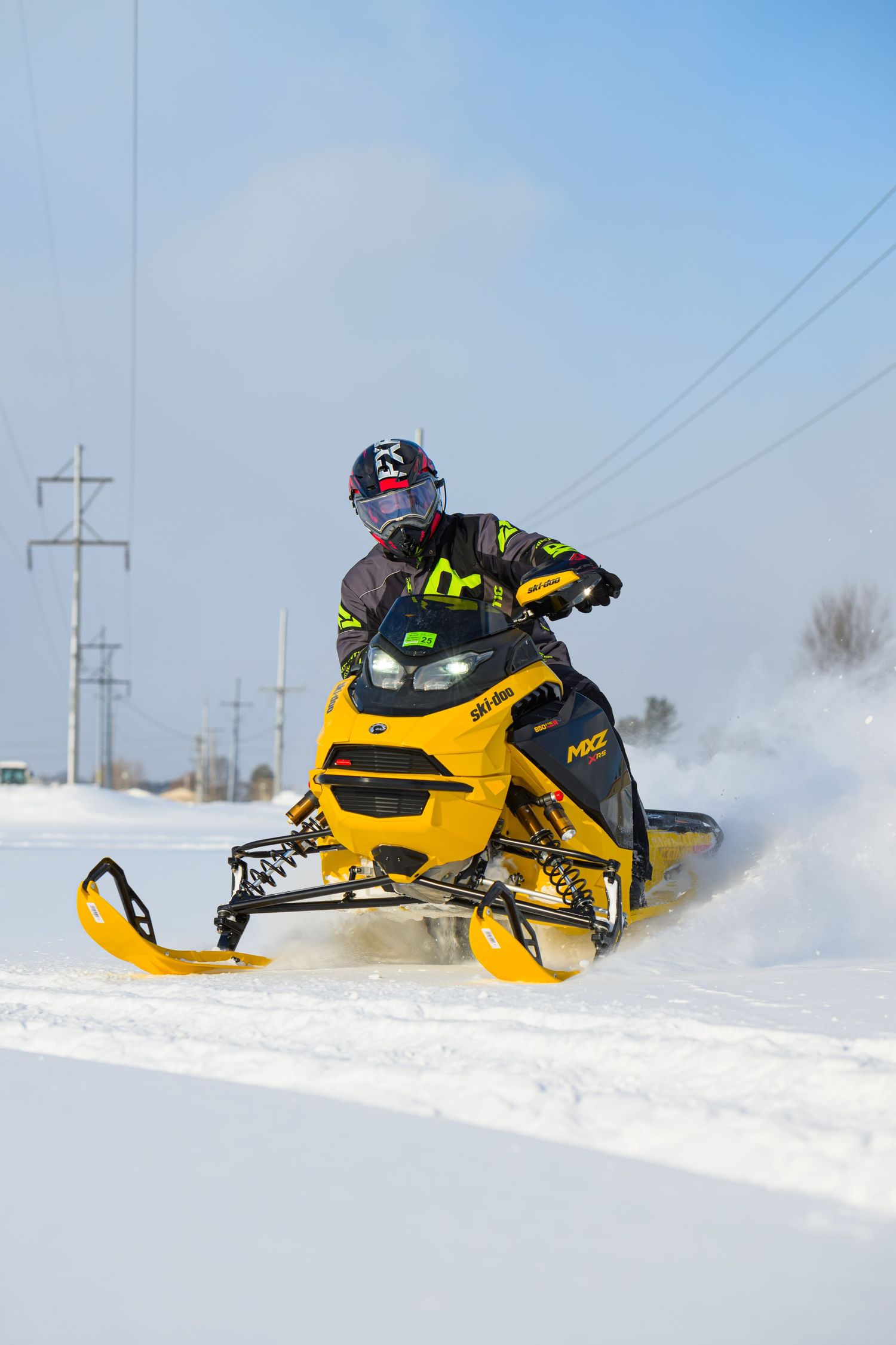 Rider on yellow Ski-Doo snowmobile speeding through snow on a bright sunny winter day.