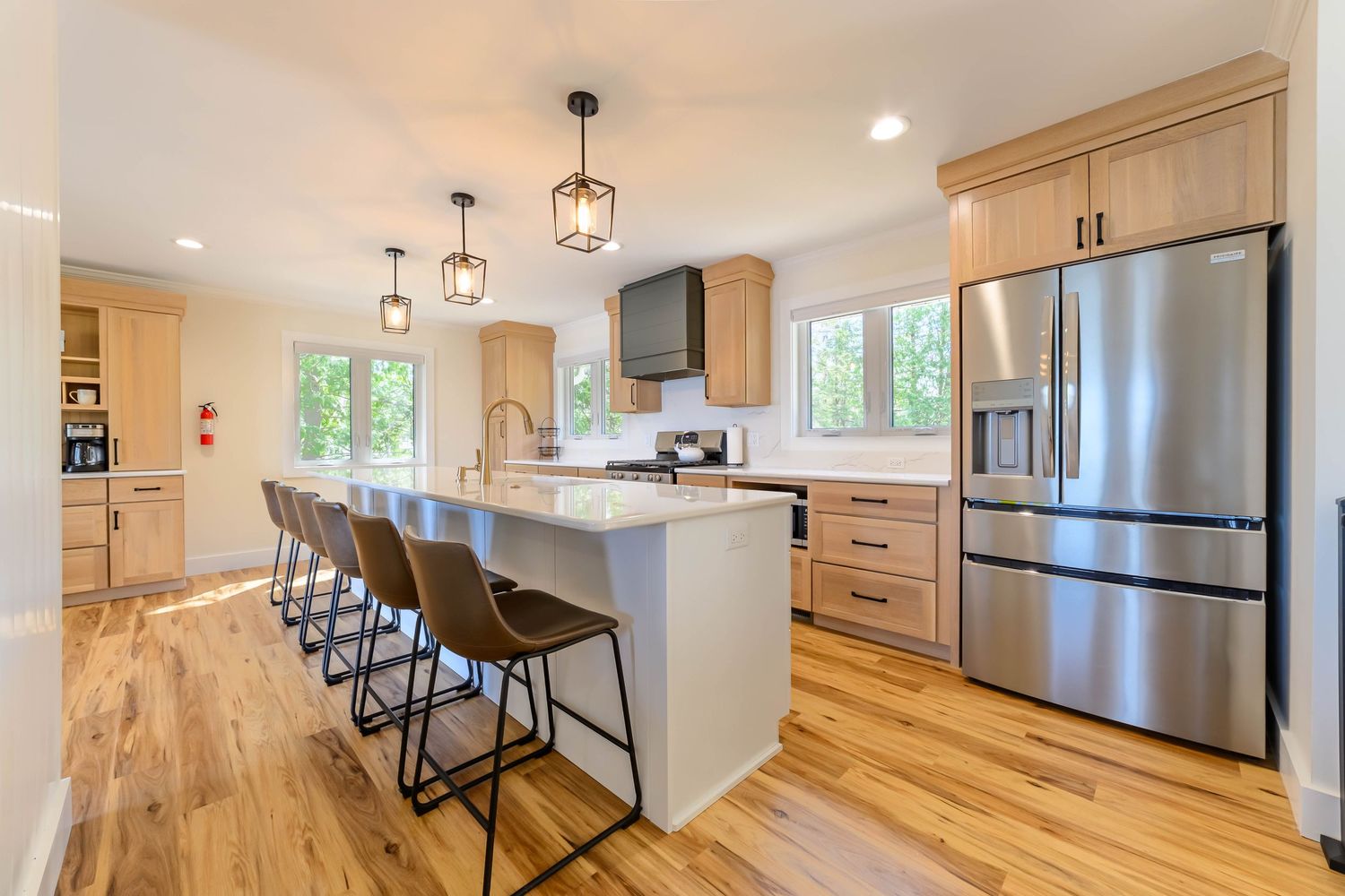 Modern kitchen with light wood cabinets, large island with bar seating, pendant lights, and stainless steel appliances.