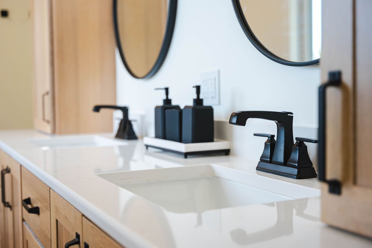 Modern bathroom double vanity with black faucets, soap dispensers, round mirrors, and white quartz countertop.